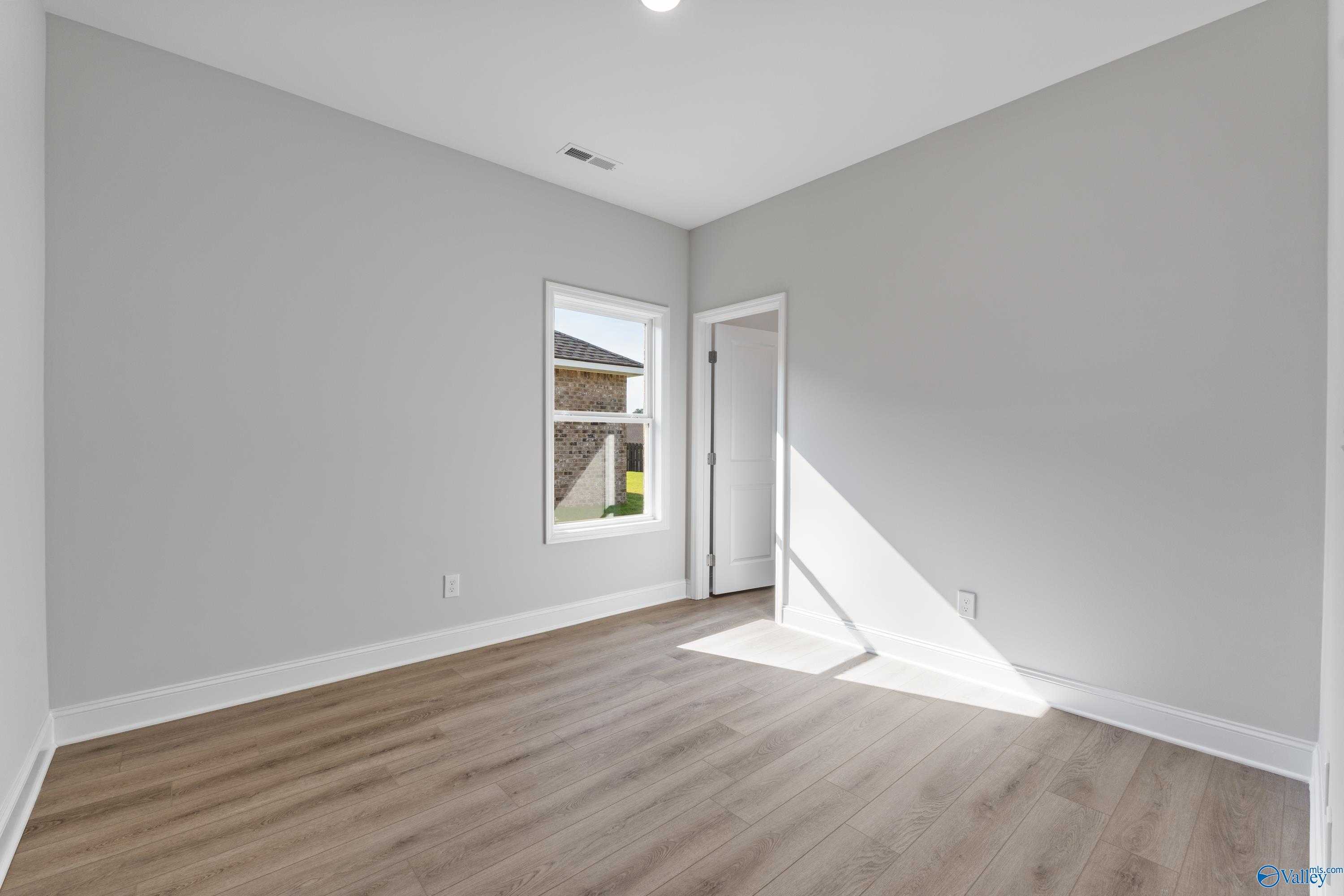 Bright bedroom featuring light gray walls, hardwood floors, and window with yard view in Davidson Homes The Daphne, Hazel Green, AL