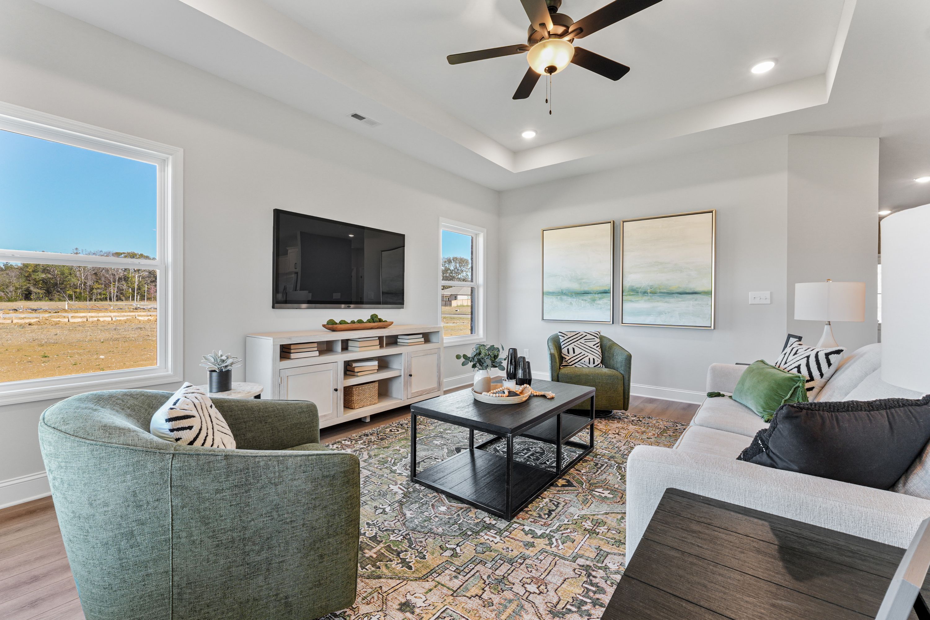 Spacious living room in Ramsay Cove, Owens Cross Roads AL featuring neutral walls, large windows with scenic views, modern green armchairs, gray sofa, and abstract art