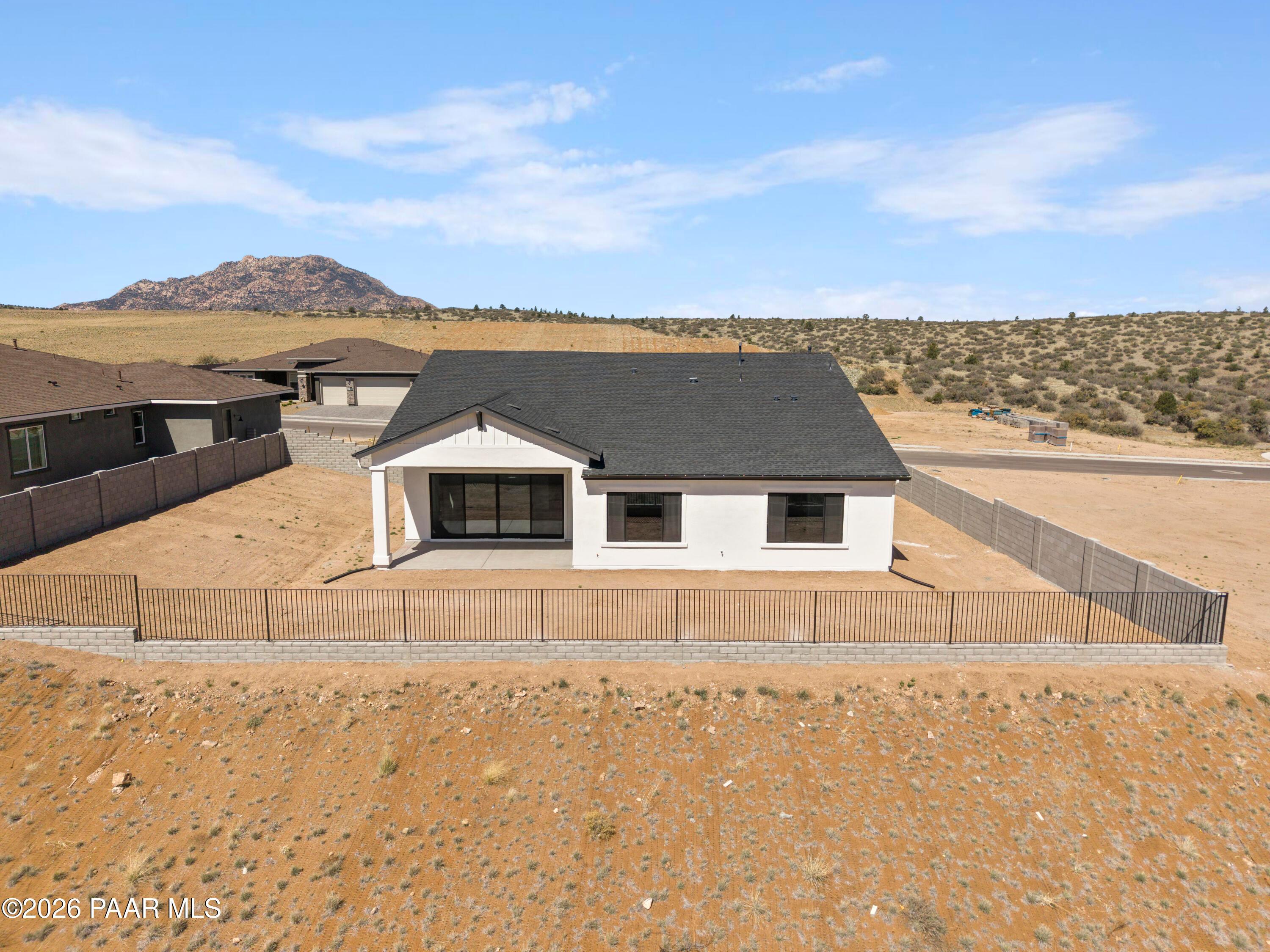 Modern white single-story 3-bedroom home with dark roof and fenced yard in Hidden Hills, Prescott, Arizona, amid desert landscape and mountains