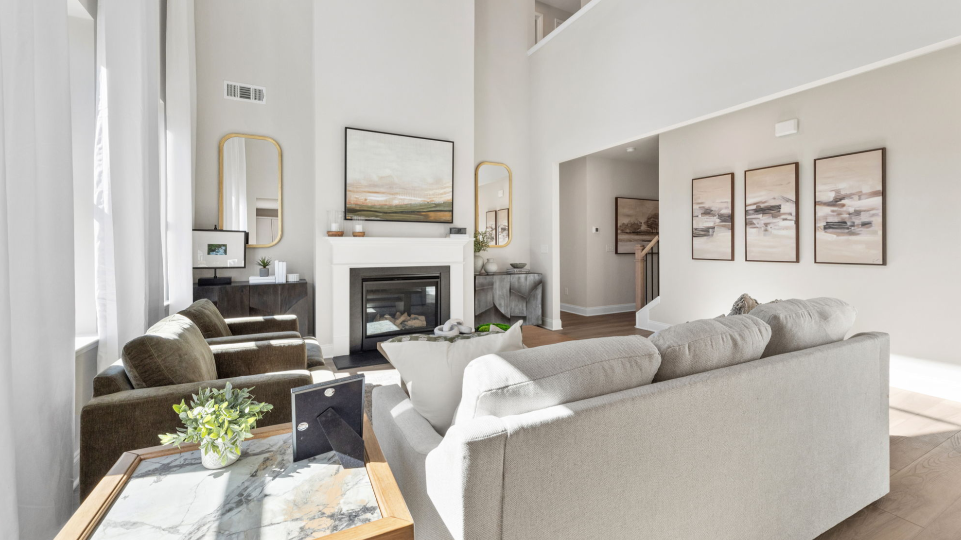 Elegant living room in Melody Lakeside Estates model home with beige sofa, green velvet chairs, marble coffee table, gas fireplace, and abstract art