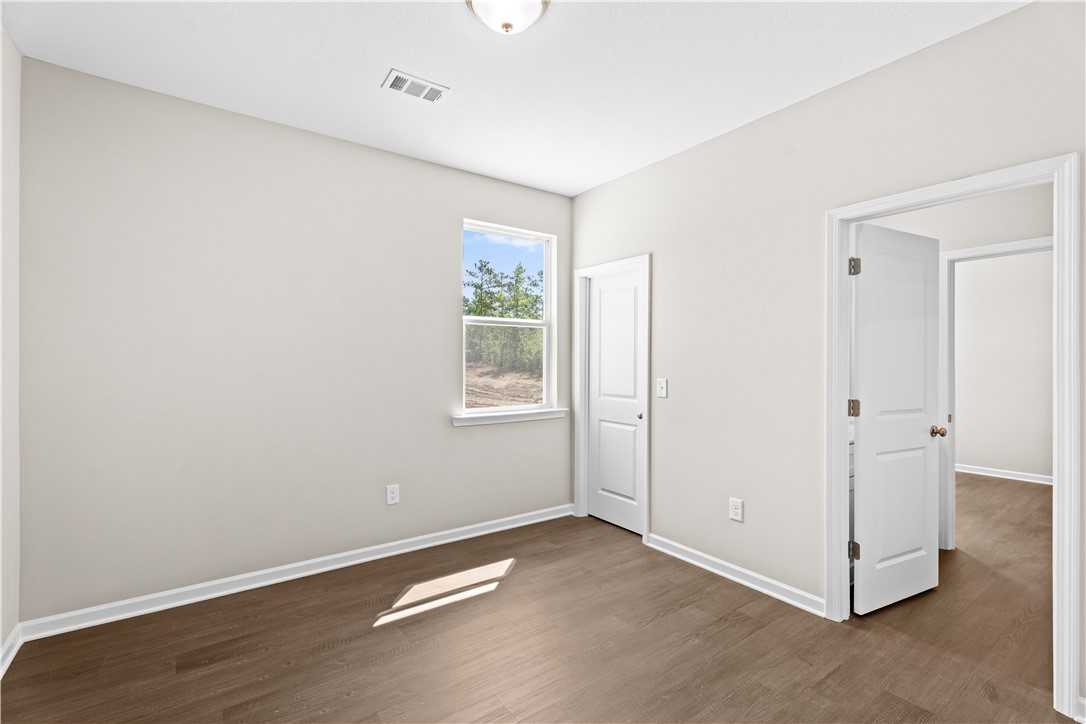 Bright bedroom with beige walls, hardwood floors, window overlooking trees in The Orion by Evermore Homes, Cusseta, Alabama