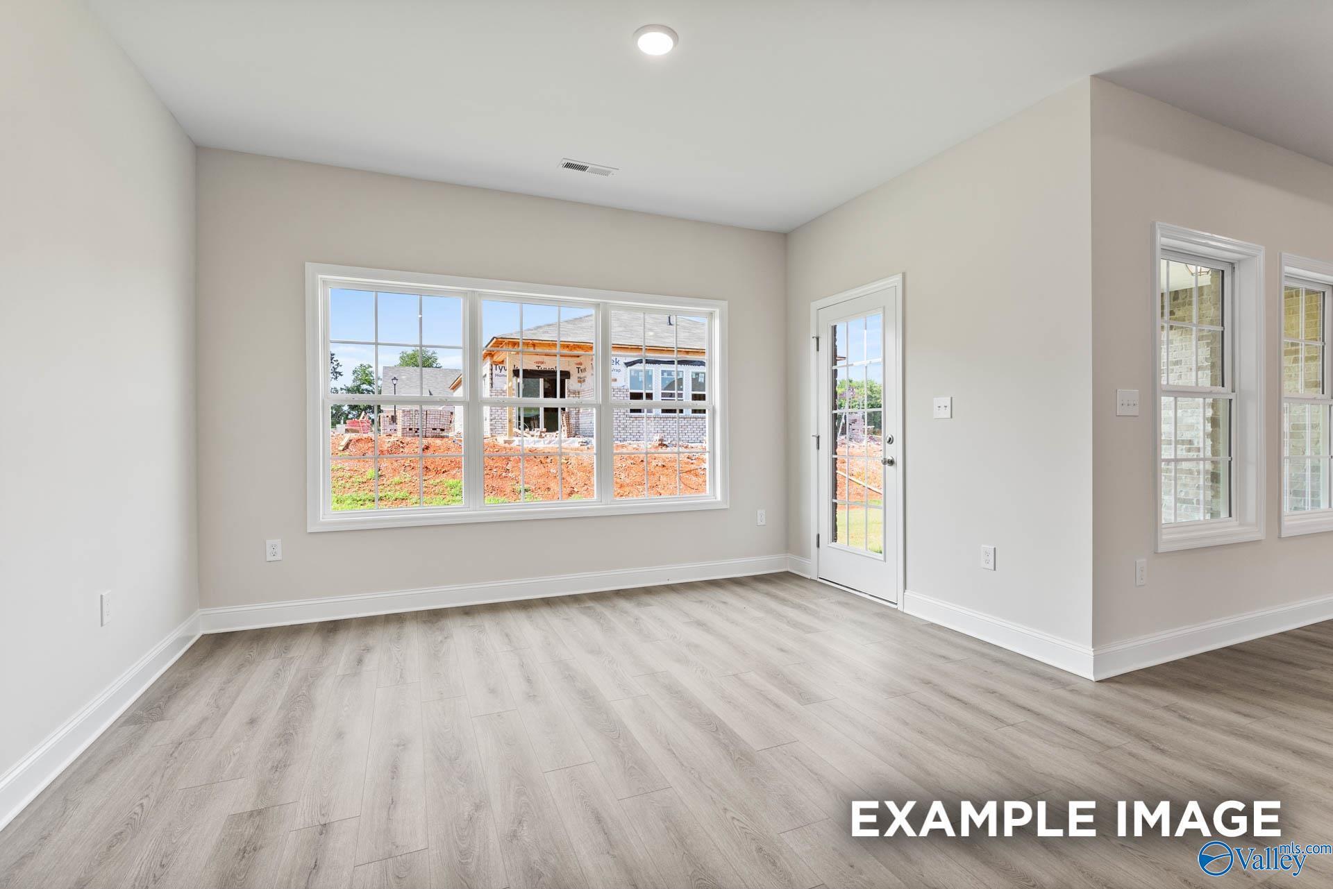 Bright living room with large windows overlooking construction site, beige walls, and light hardwood floors in The Finleigh by Davidson Homes, Huntsville AL