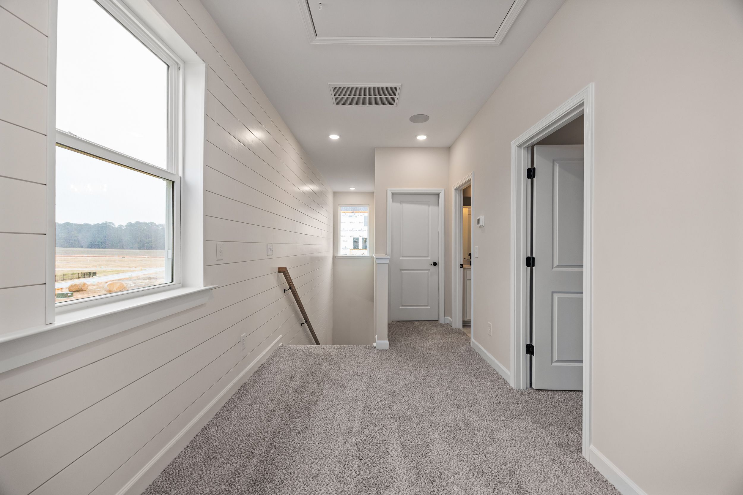 Spacious upstairs hallway in Forestville Yard home, Knightdale NC with white shiplap walls, carpet flooring and large windows