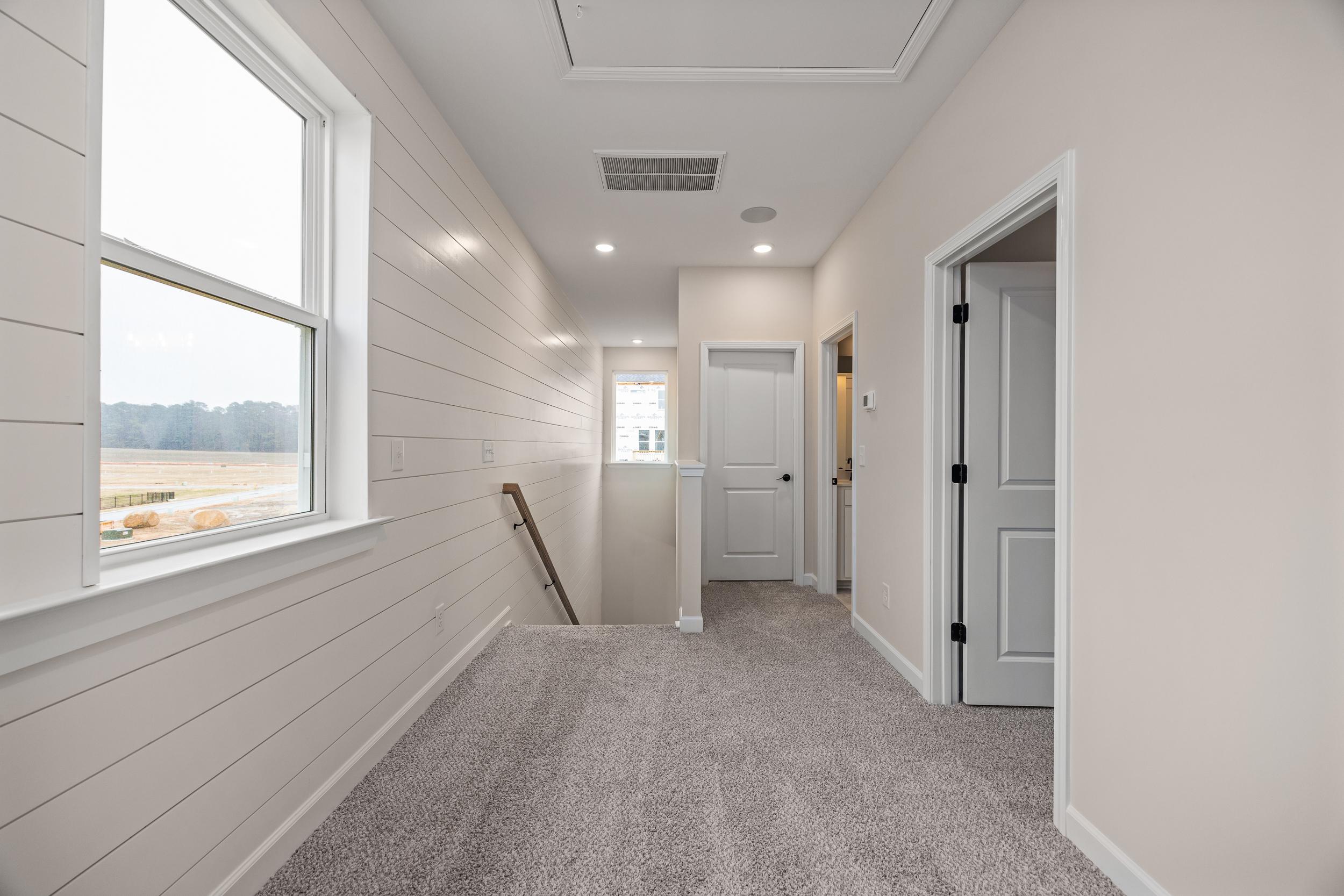 Spacious upstairs hallway in Forestville Yard home, Knightdale NC with white shiplap walls, carpet flooring and large windows