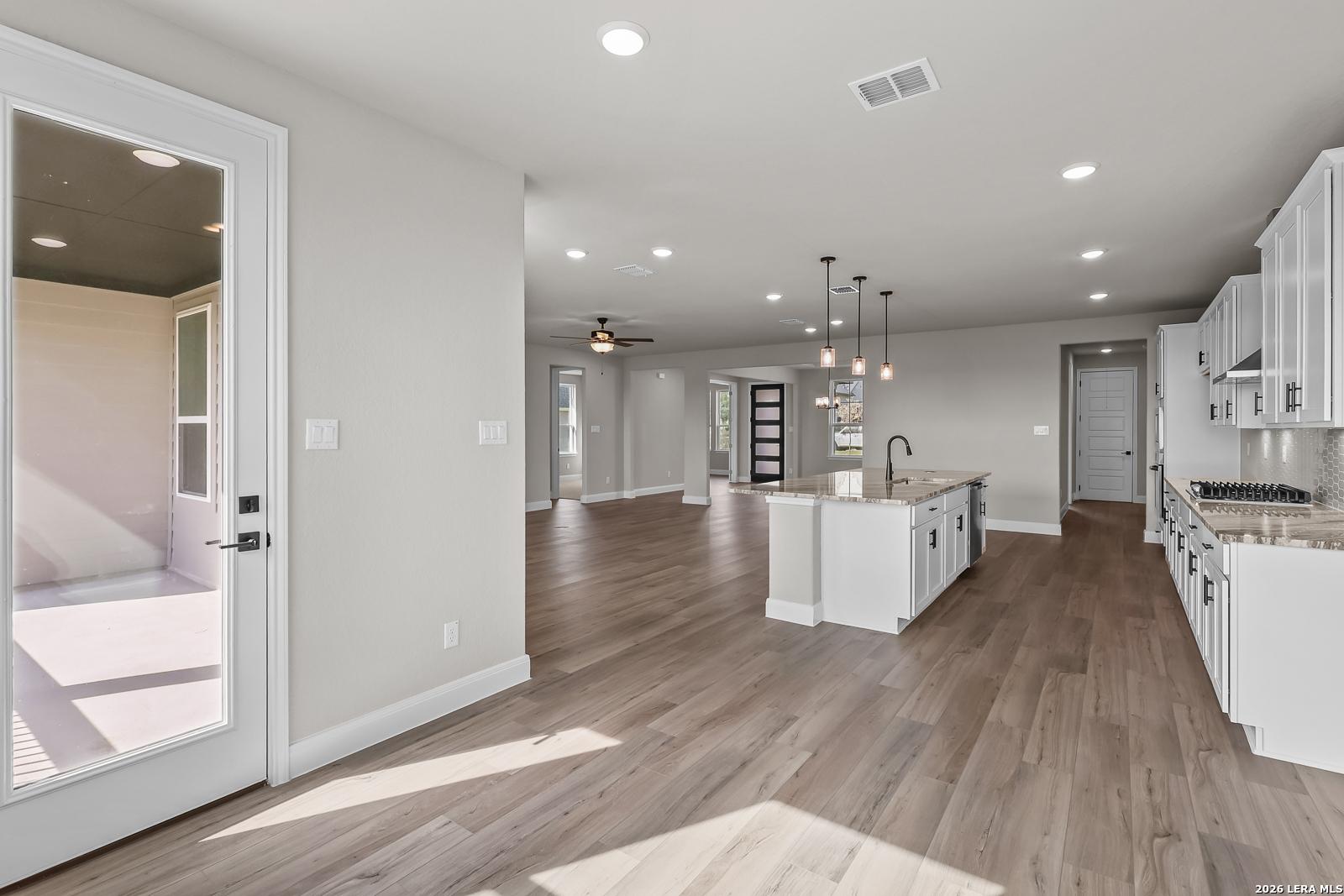 Open-concept kitchen with white cabinetry, granite island, and wood-look floors in Davidson Homes The Foster E, Castroville, Texas