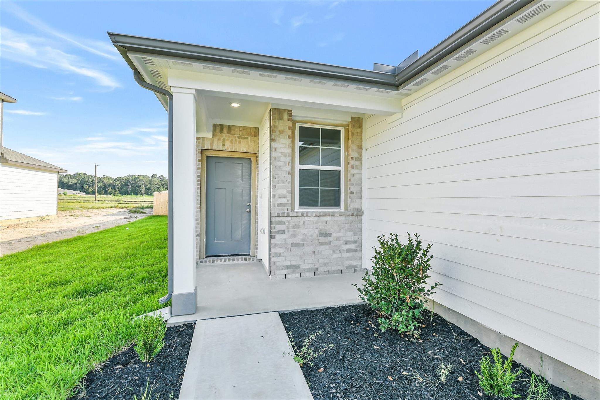 Modern front entrance of Davidson Homes Colorado F in Liberty Estates, Cleveland, Texas with brick accents, white columns, and landscaped walkway