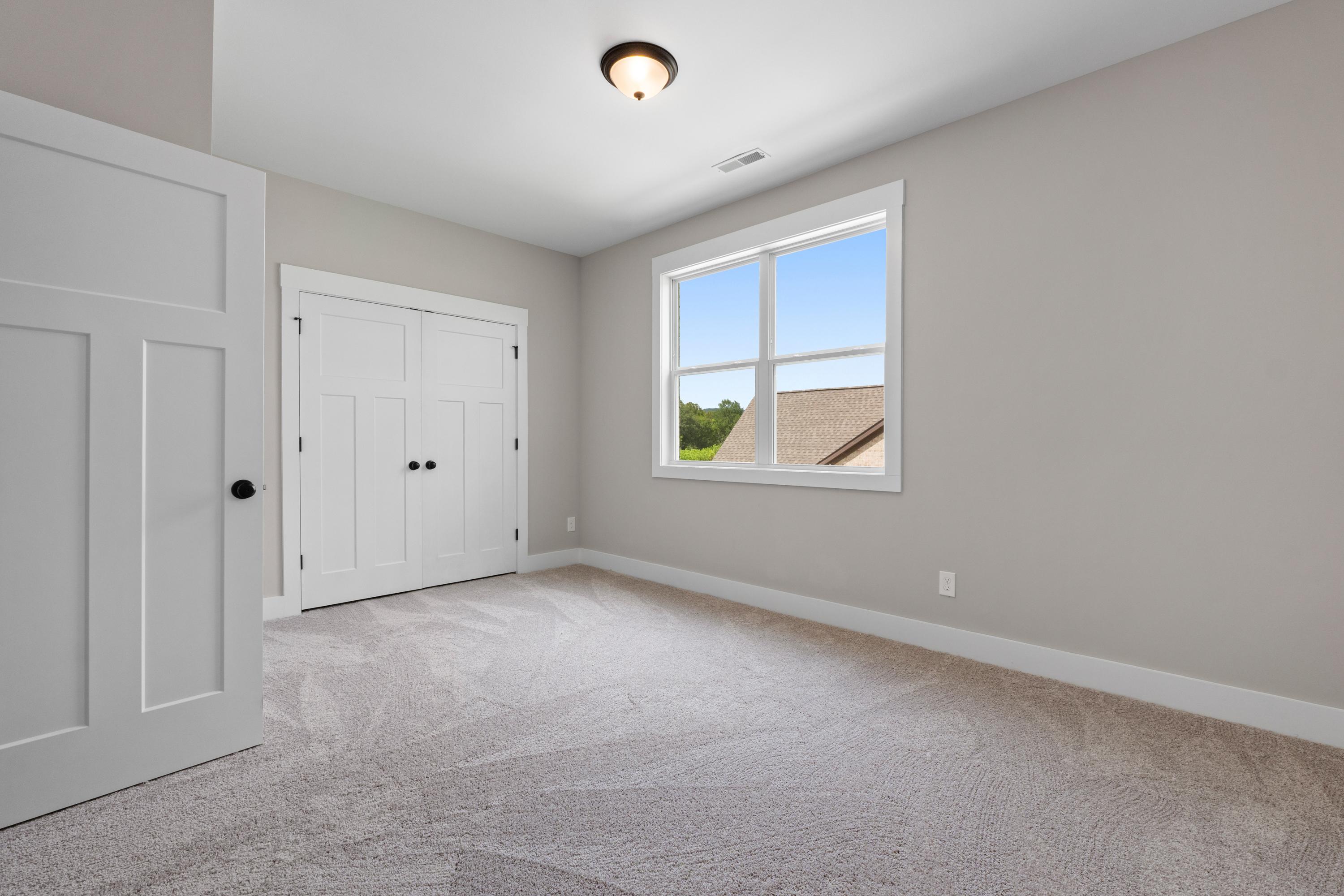 Spacious bedroom in The Oxford home design by Evermore Homes with light gray walls, white double doors, large window, and plush carpet