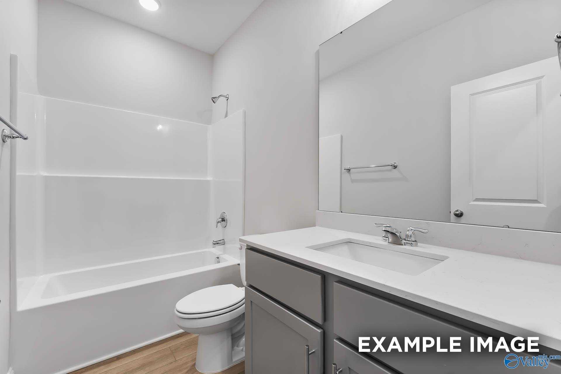 Modern guest bathroom featuring white tub shower combo, gray double vanity, and large mirror in Davidson Homes The Franklin C, Athens, Alabama