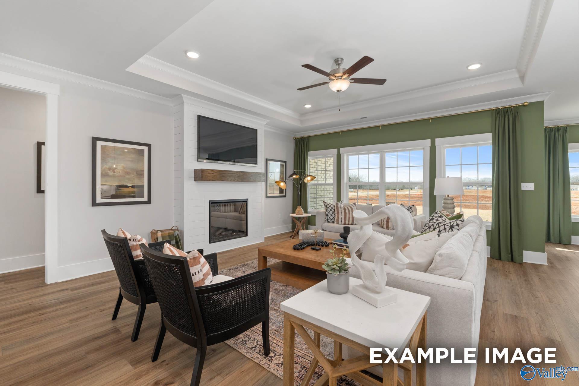 Cozy living room with fireplace, TV mantel, white sofas, ceiling fan, and large windows in Davidson Homes The Finleigh, Decatur, Alabama