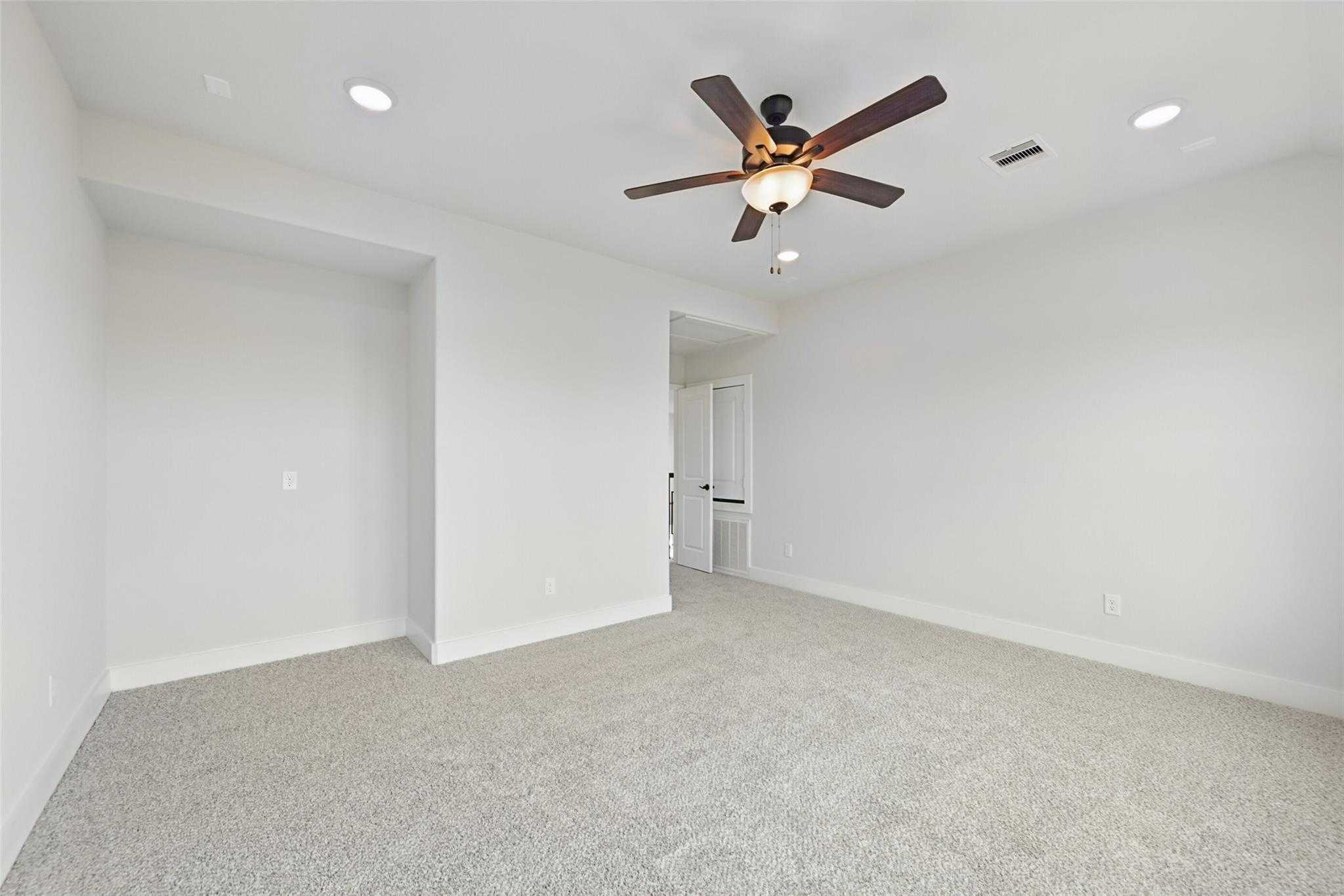 Spacious bedroom with beige carpet, white walls, ceiling fan and recessed lights in Davidson Homes The Victoria C, Texas City