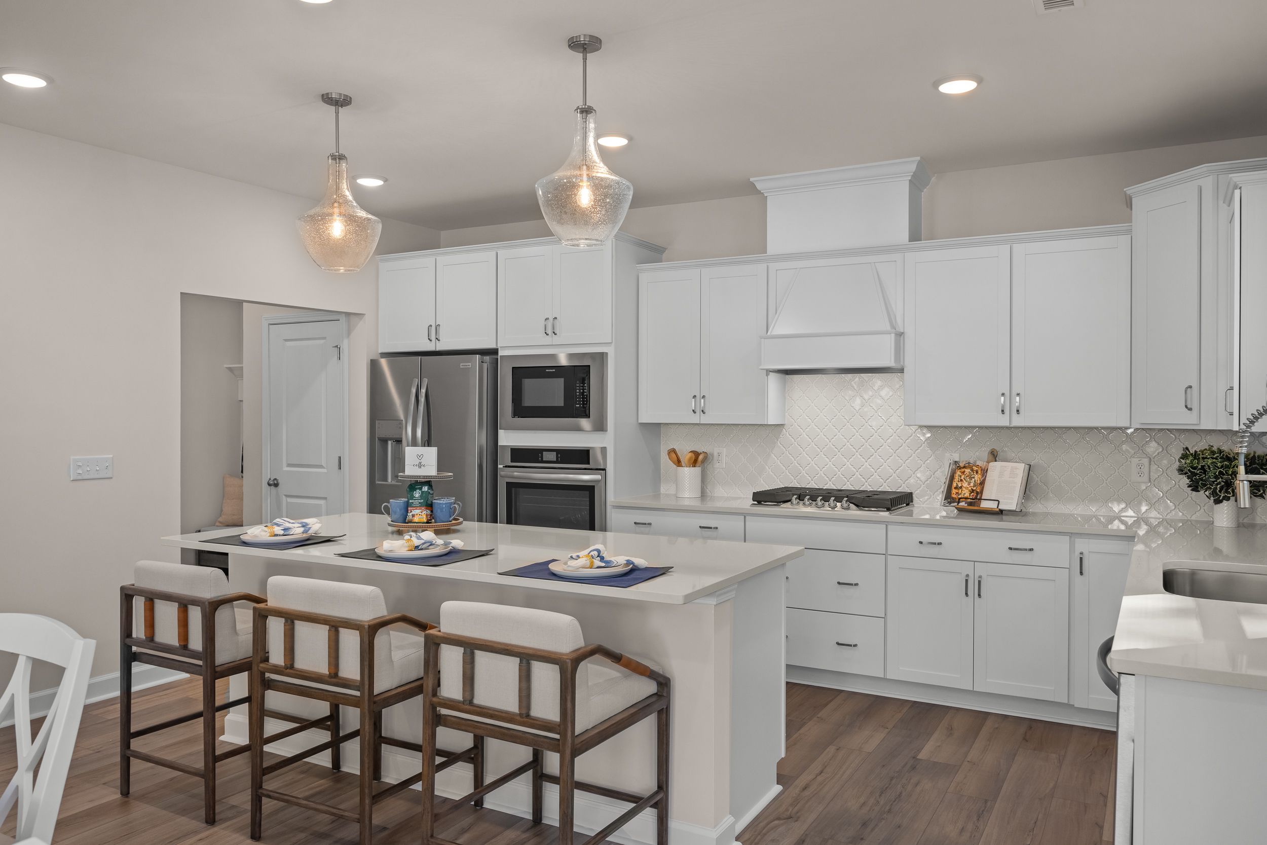 Modern kitchen in The Hickory II A featuring white cabinets, large island with bar stools, stainless appliances, and wood flooring