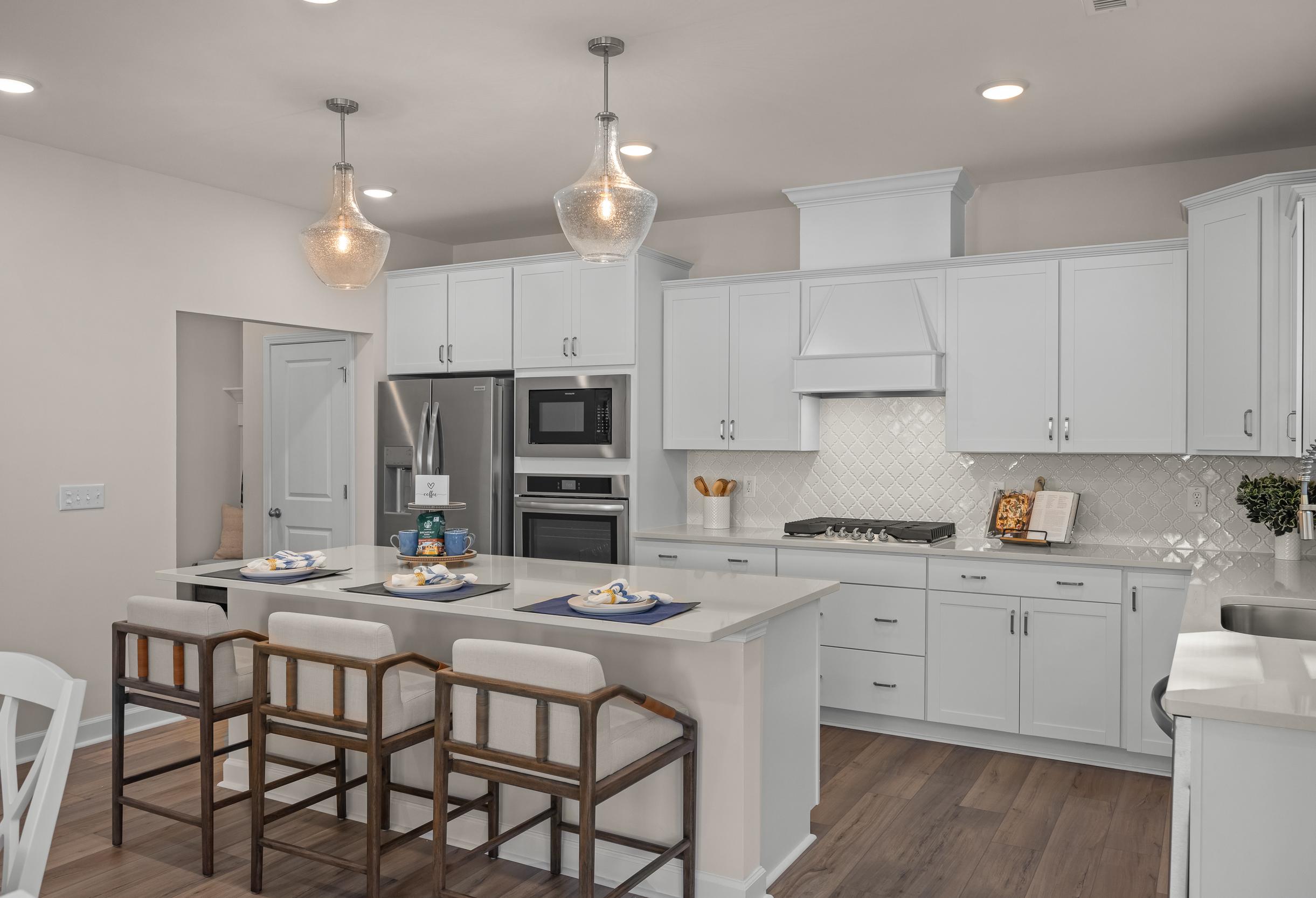 Modern kitchen in The Hickory II A featuring white cabinets, large island with bar stools, stainless appliances, and wood flooring
