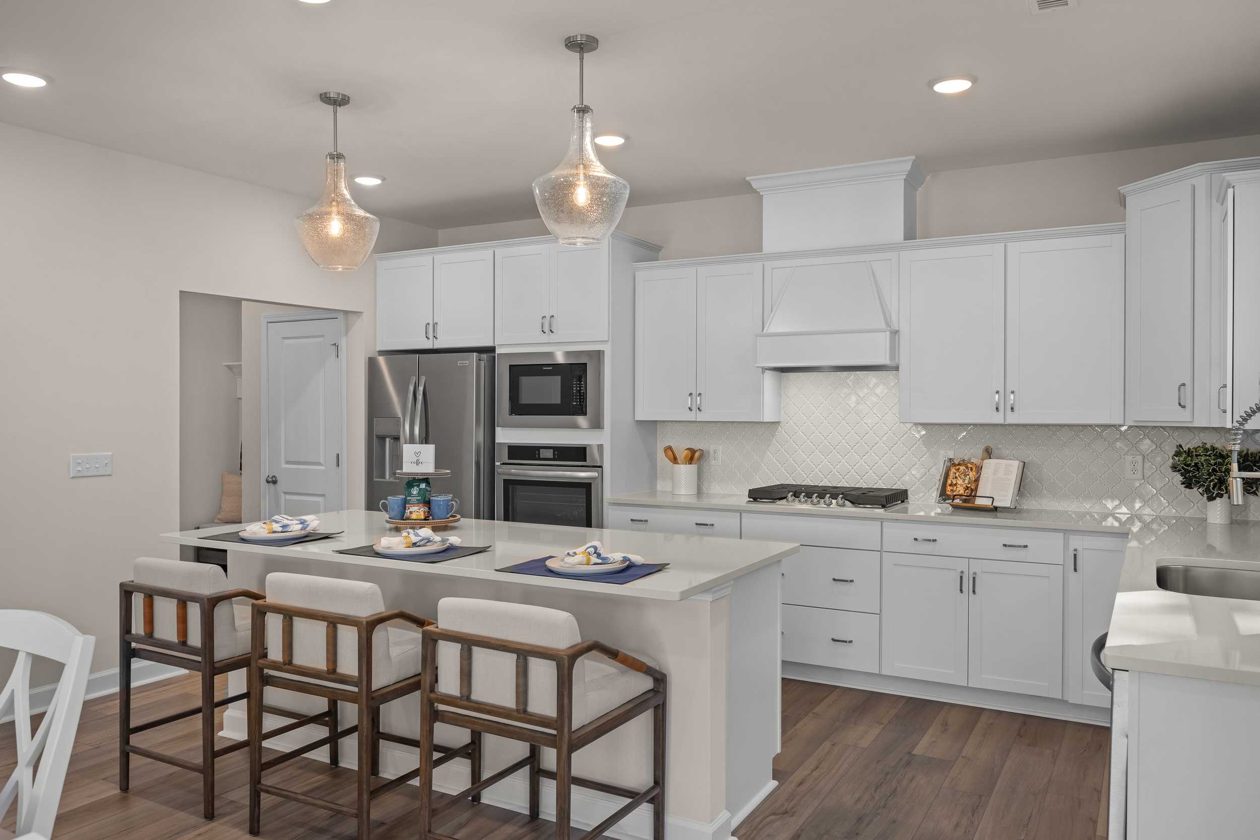 Spacious gourmet kitchen in The Hickory II E with white shaker cabinets, quartz island, stainless appliances, and pendant lights