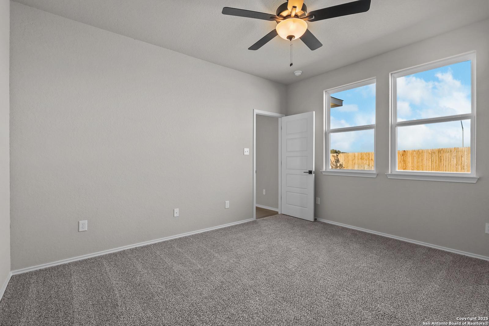 Bright secondary bedroom with ceiling fan, gray walls, and windows to fenced backyard in The Brazos C home, San Antonio