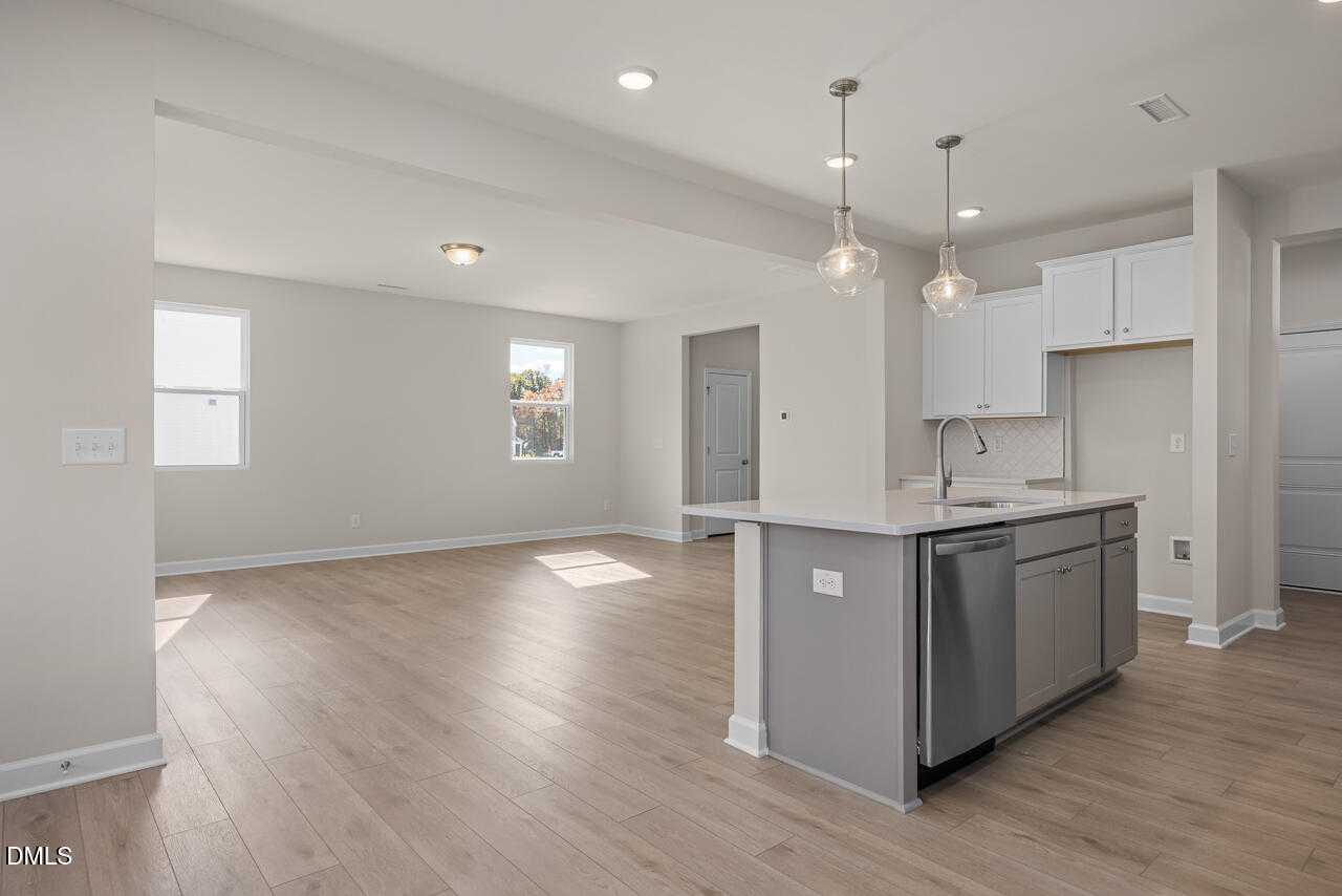 Open-concept kitchen with quartz island, stainless dishwasher, pendant lights, and hardwood floors in The Gavin C home, Lillington, NC
