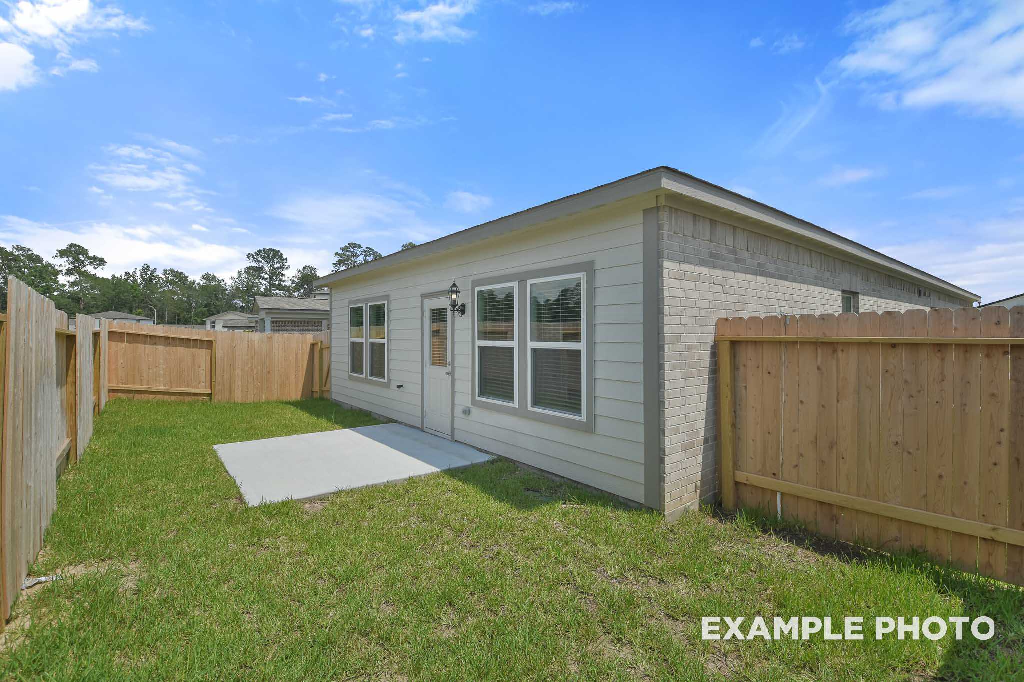 The Comal single-story home exterior with beige siding, brick base, covered patio, and fenced grassy yard in Magnolia, Texas