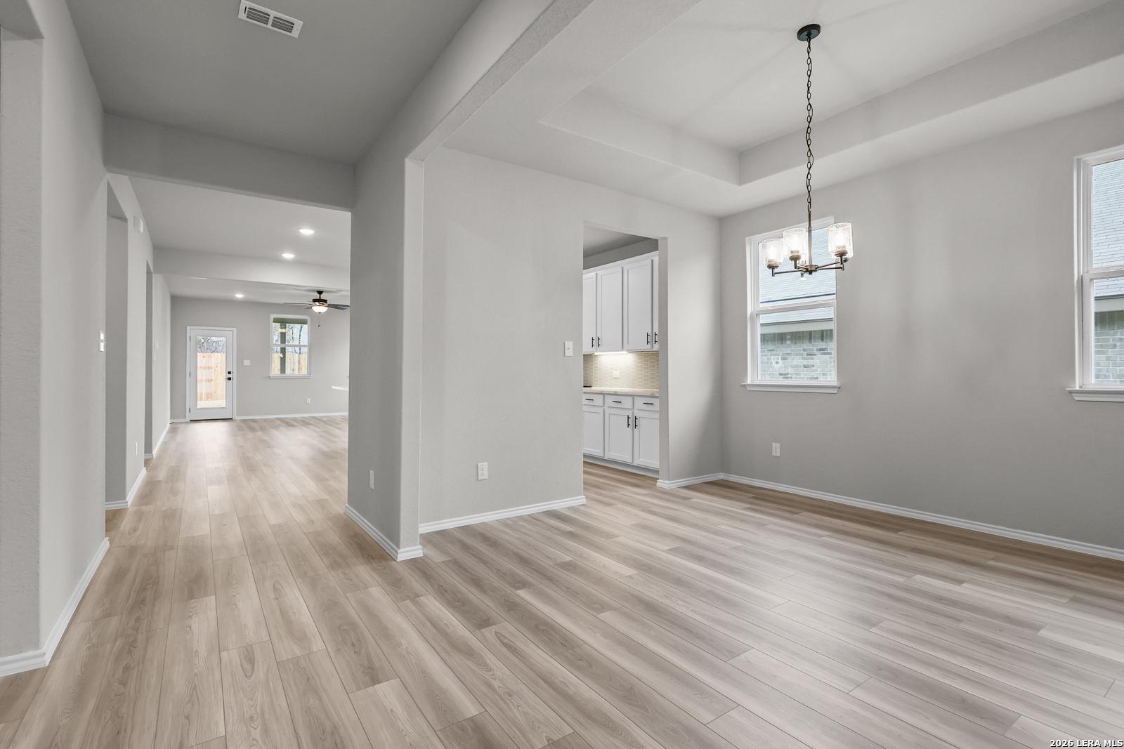 Open entry hallway with light oak floors leading to chandelier-lit dining and white cabinet kitchen in Davidson Homes The Glenwood F, San Antonio