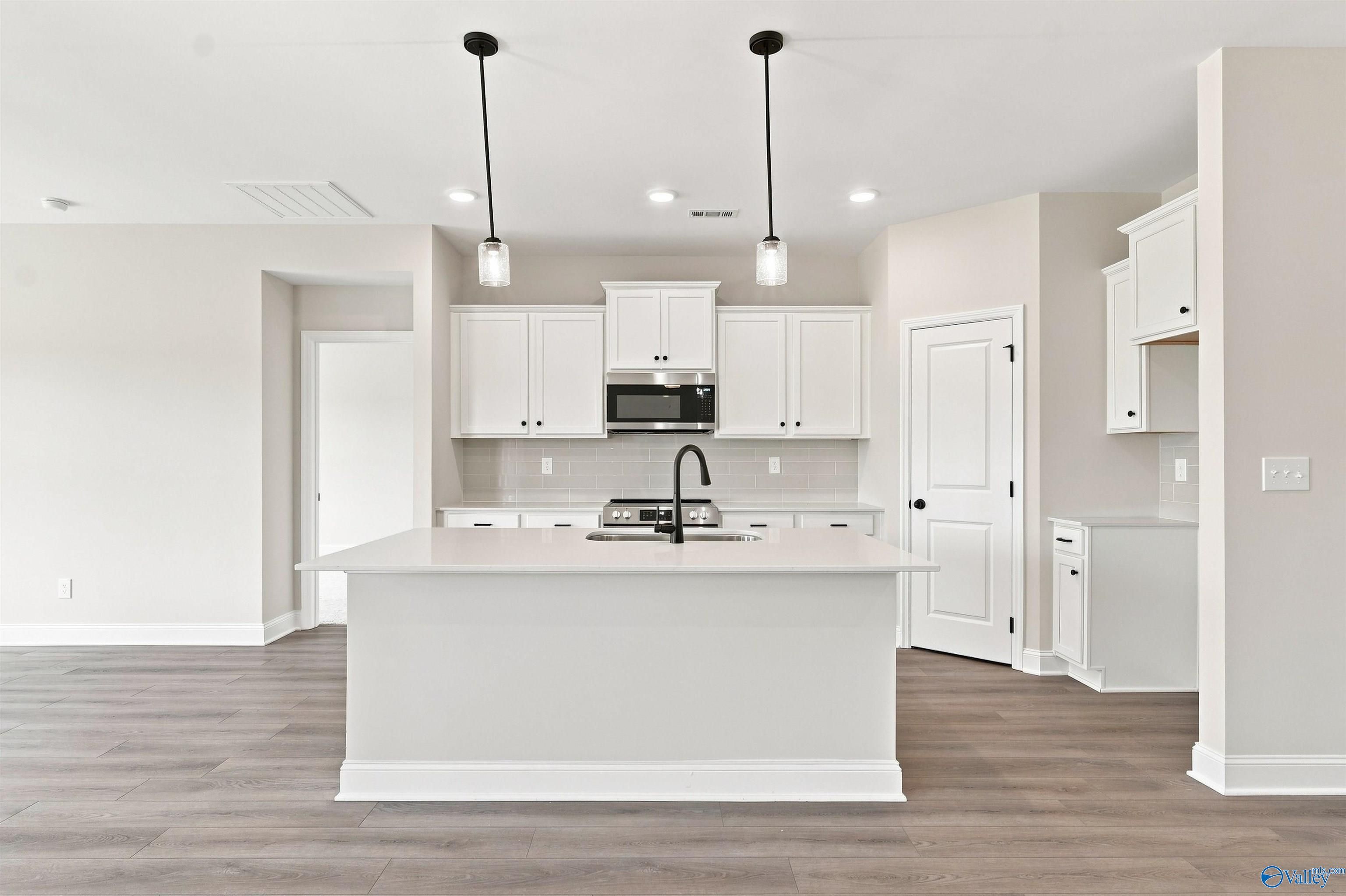 Bright white kitchen with center island, black pendant lights, and stainless appliances in Davidson Homes The Everett B, Toney AL