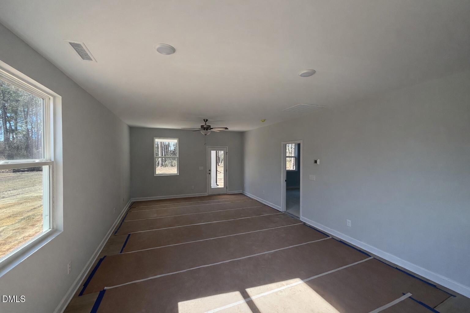 Spacious empty great room with gray walls, large windows, ceiling fan in Davidson Homes The Carter C, Lillington, NC
