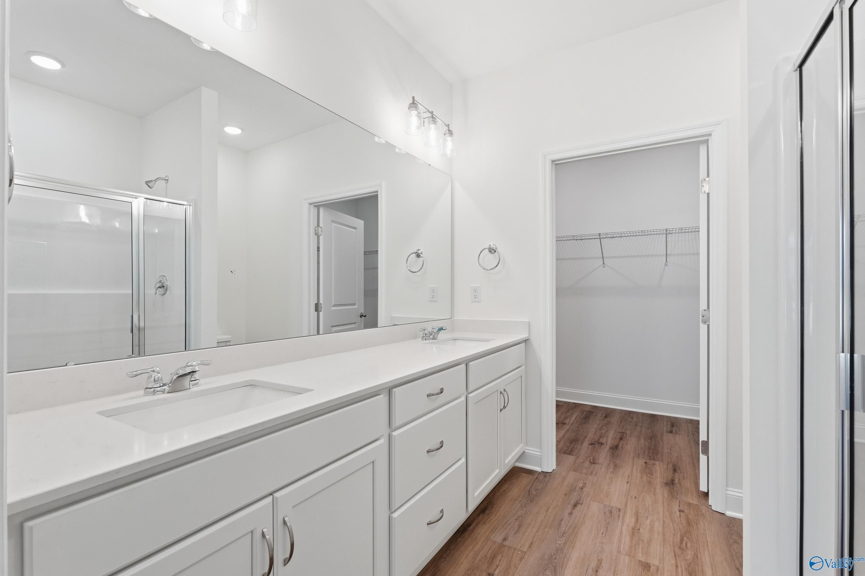 Modern master bathroom with white double vanity, quartz countertop, glass shower, and adjacent closet in Davidson Homes Cumberland D, Decatur AL