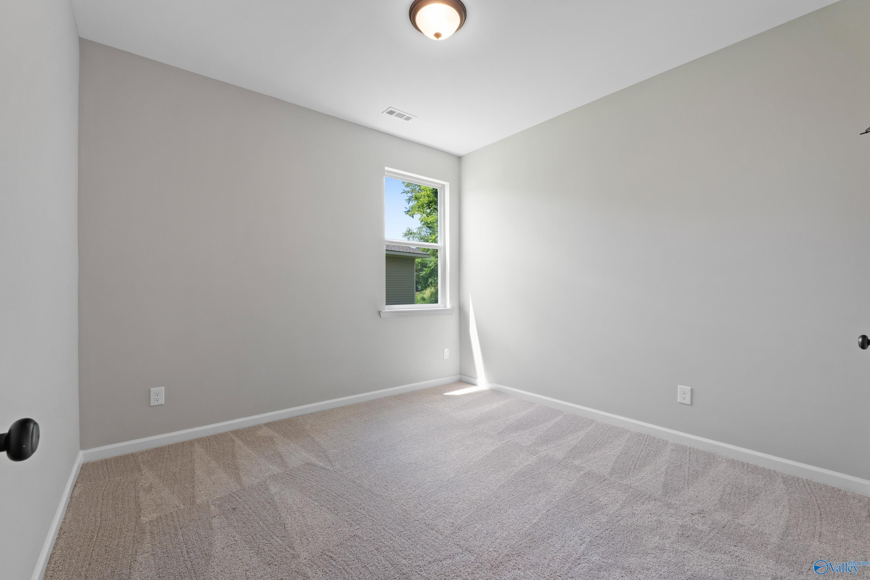Bright empty secondary bedroom with light gray walls, carpet floor, and sunny window in Davidson Homes The Phoenix, Hazel Green