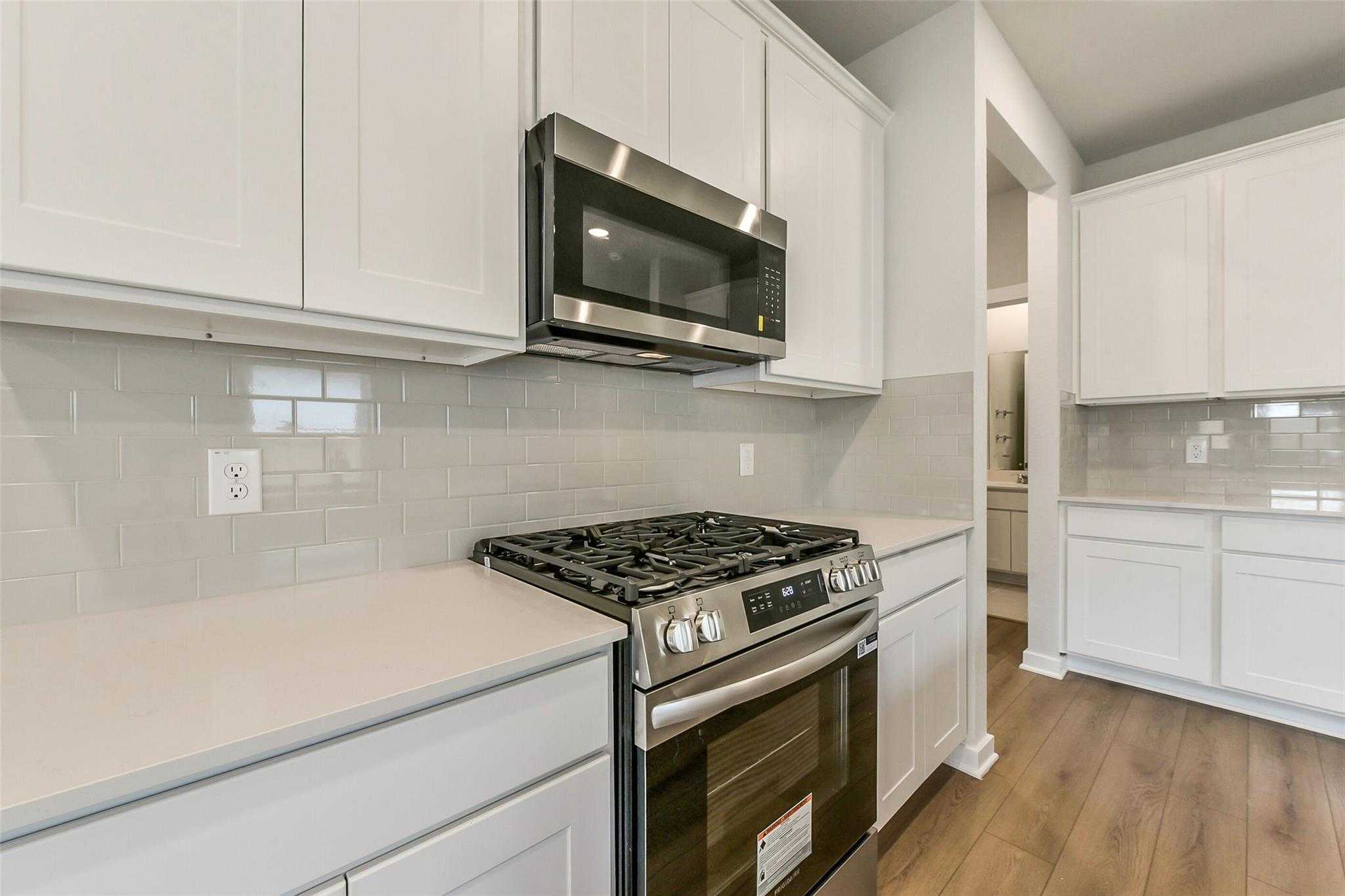 Modern kitchen featuring white shaker cabinets, stainless steel gas range, microwave, and quartz counters in The Frio G floor plan, Dayton Texas