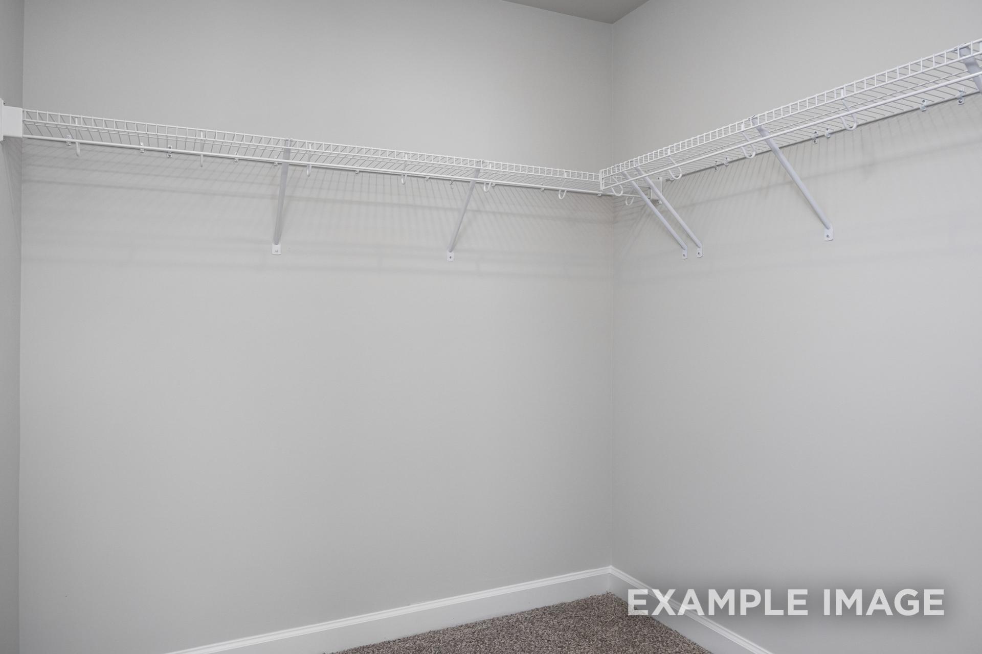 Spacious walk-in closet in The Preston B master suite featuring white wire shelving on light gray walls