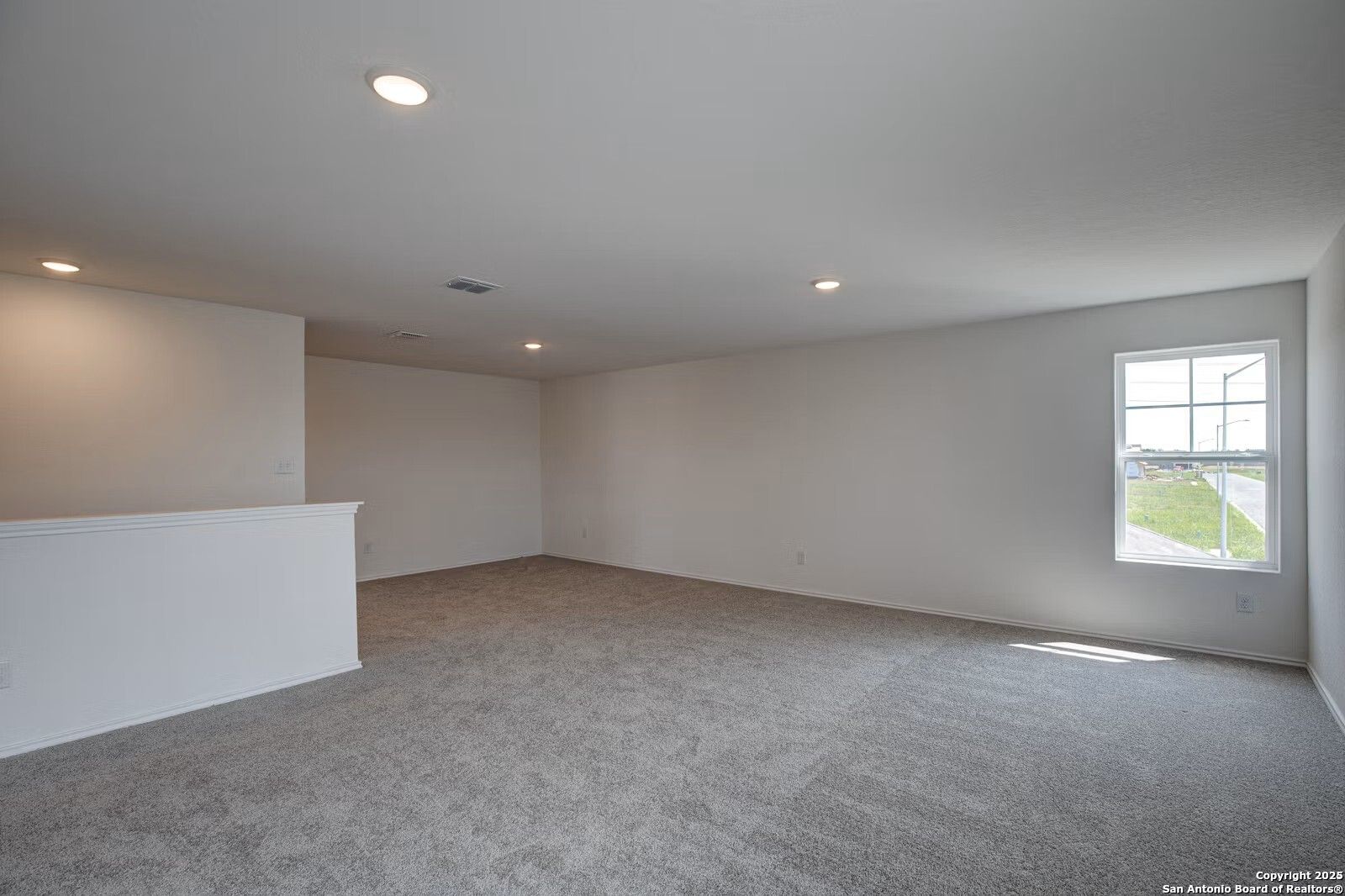 Spacious upstairs loft with gray carpet, neutral walls, large window, and balcony railing in The Douglas B home, Seguin, Texas