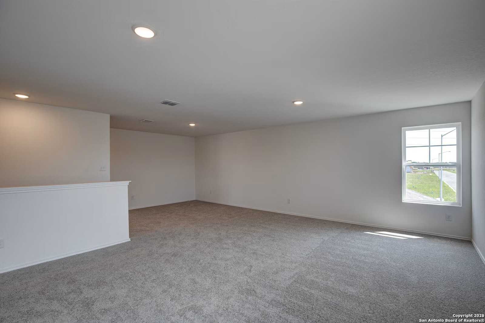 Spacious upstairs loft with gray carpet, neutral walls, large window, and balcony railing in The Douglas B home, Seguin, Texas