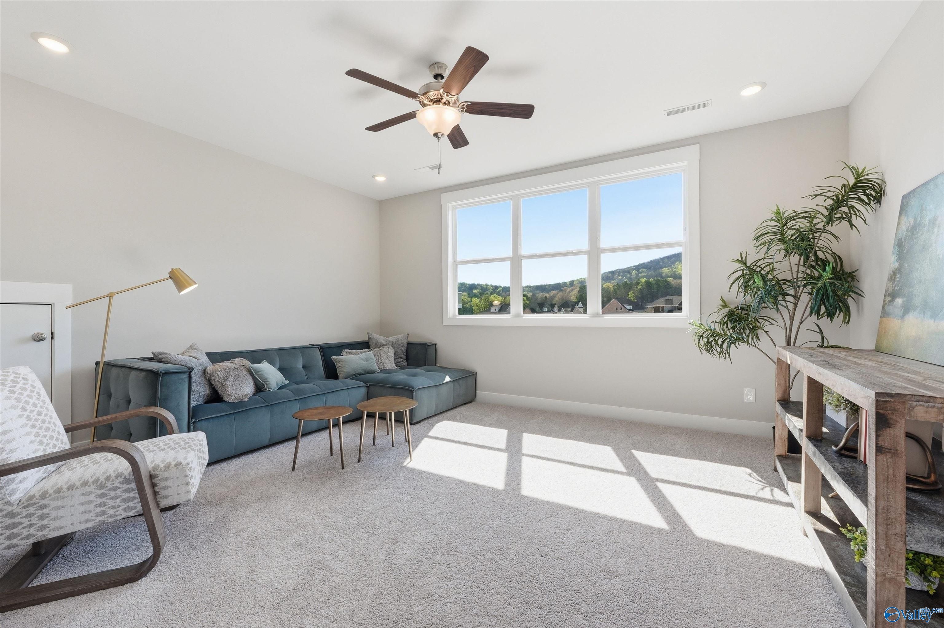 Cozy living room with blue velvet sectional sofa, large windows overlooking green hills, ceiling fan in Evermore Homes The Oxford B, Owens Cross Roads, AL