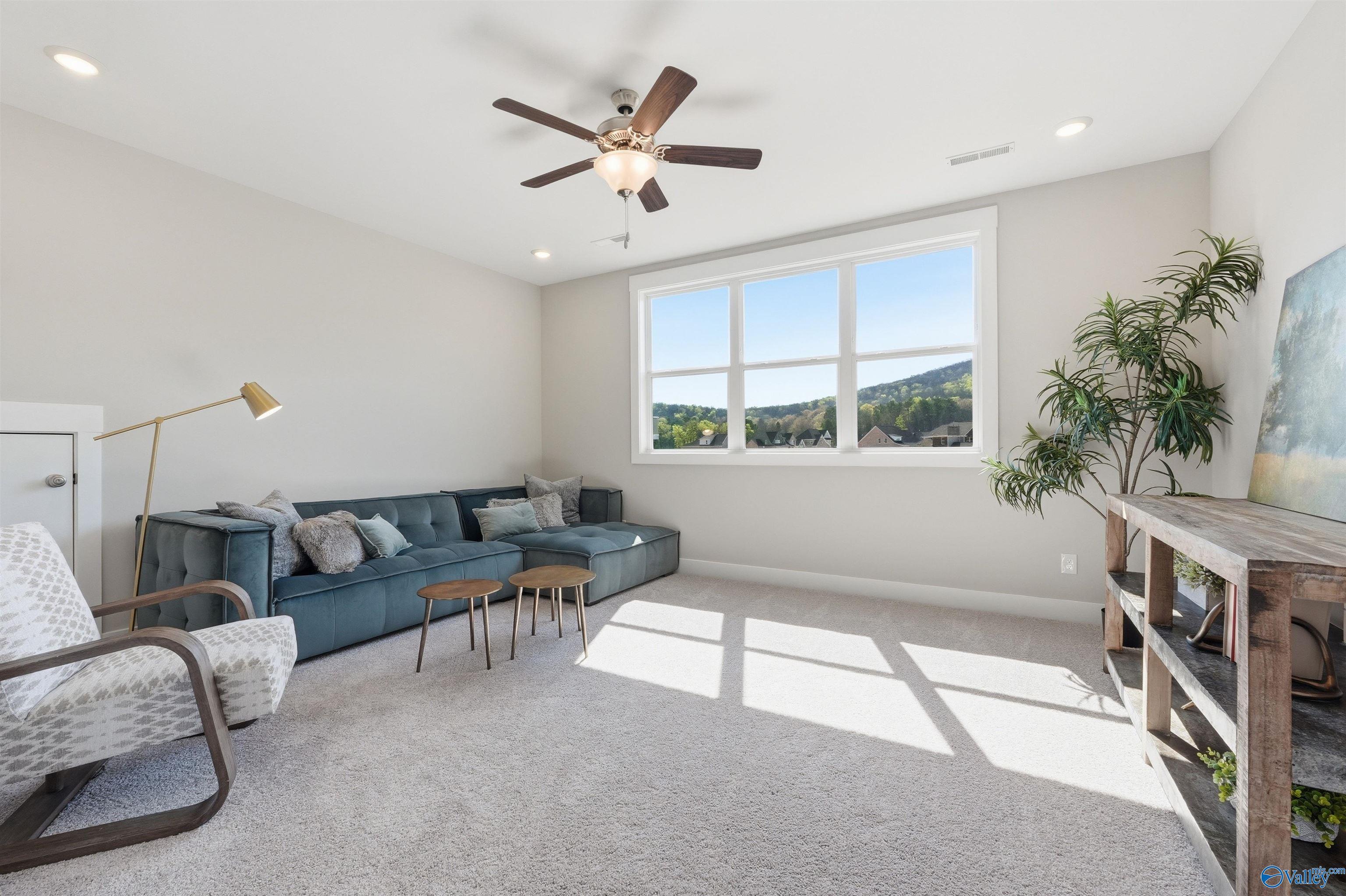 Cozy living room with blue velvet sectional sofa, large windows overlooking green hills, ceiling fan in Evermore Homes The Oxford B, Owens Cross Roads, AL