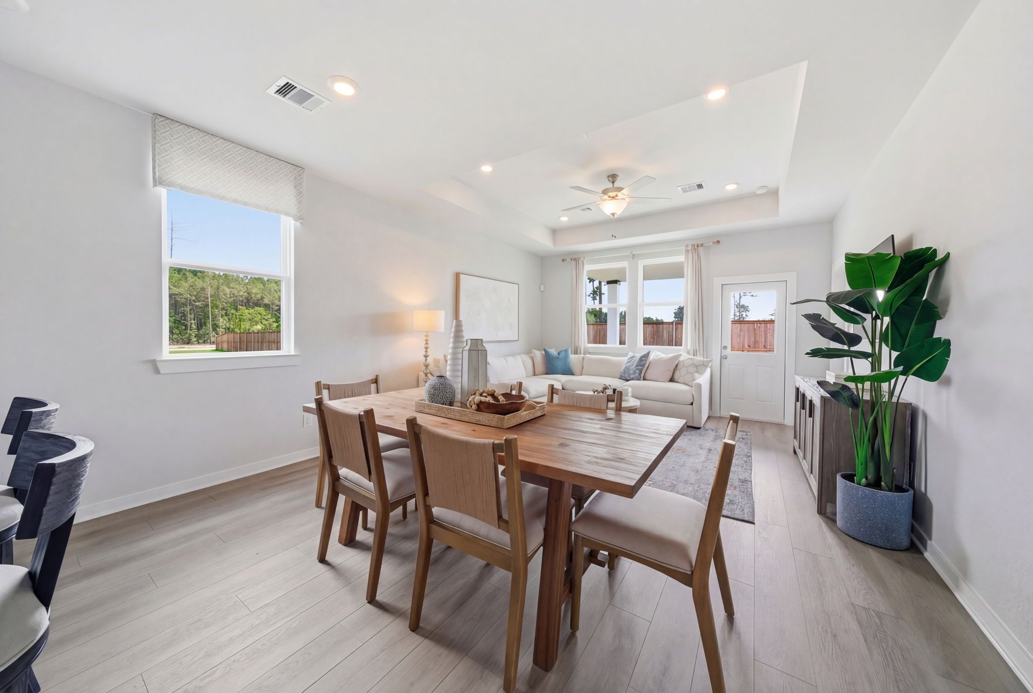 Open-concept dining area at Spring Branch Crossing in Conroe TX with wooden table, upholstered chairs, sectional sofa, potted plant, and hardwood floors