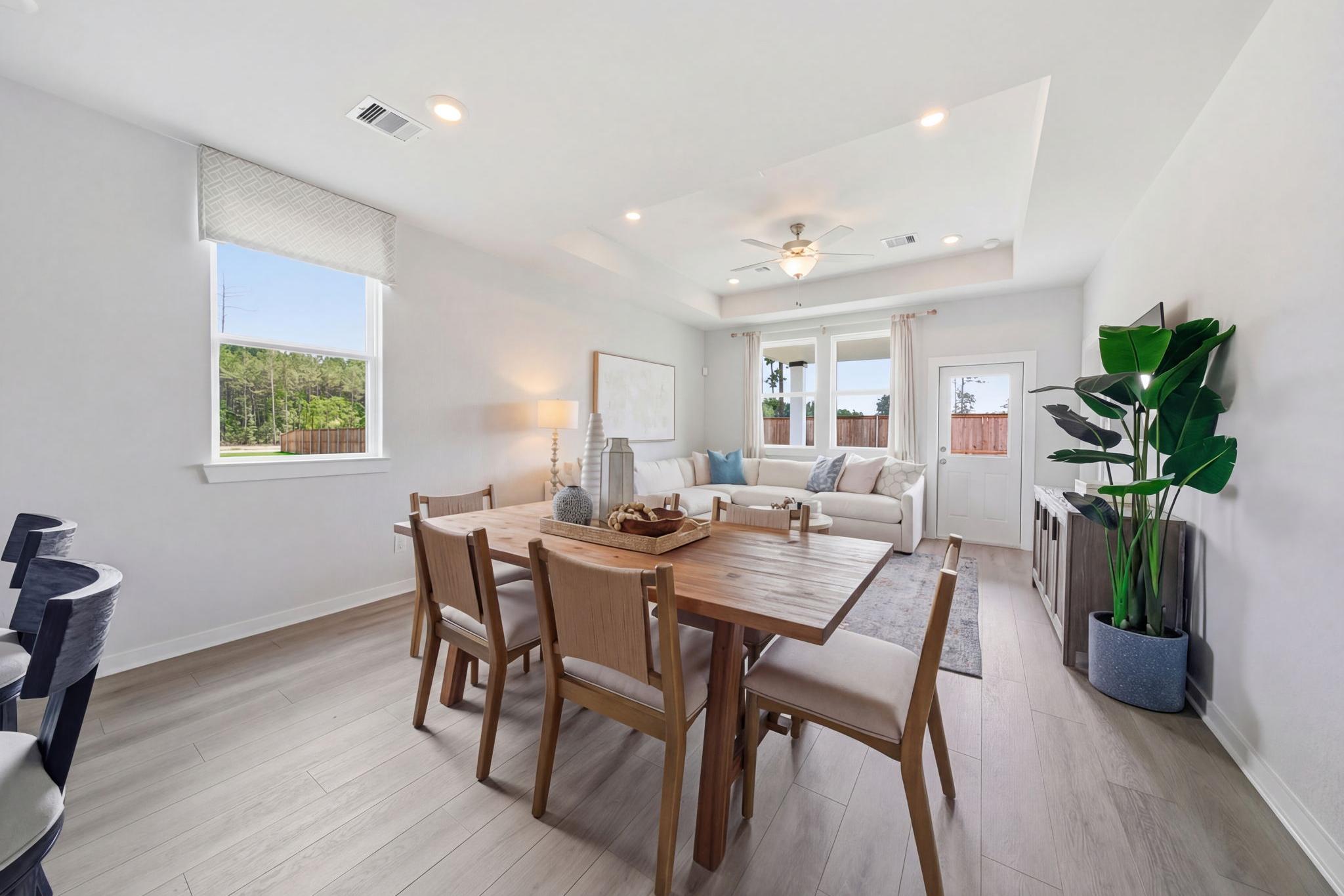 Open-concept dining area at Spring Branch Crossing in Conroe TX with wooden table, upholstered chairs, sectional sofa, potted plant, and hardwood floors