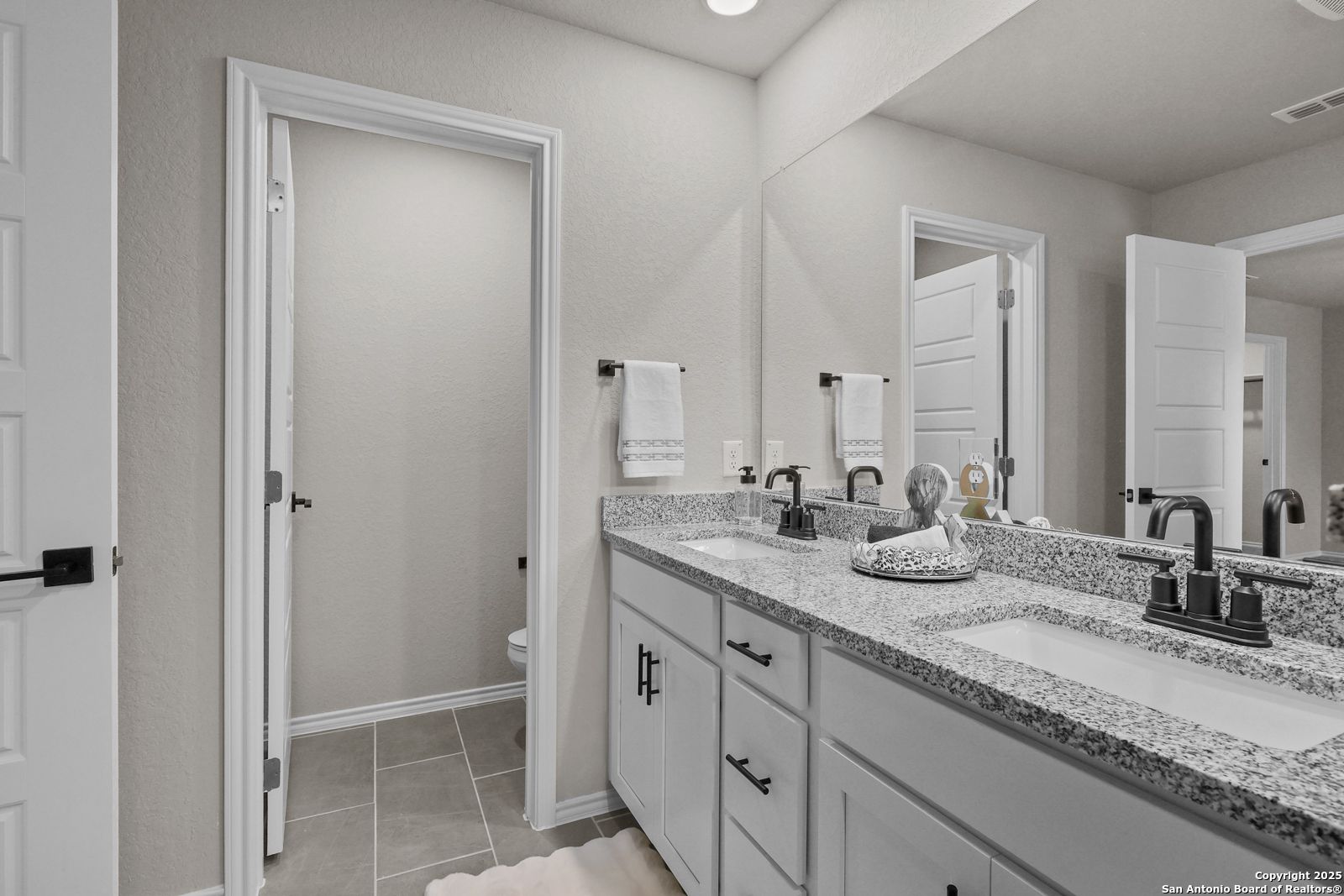 Modern master bathroom featuring double granite vanity, large mirrors, and neutral tile in Davidson Homes The Charlotte B, San Antonio