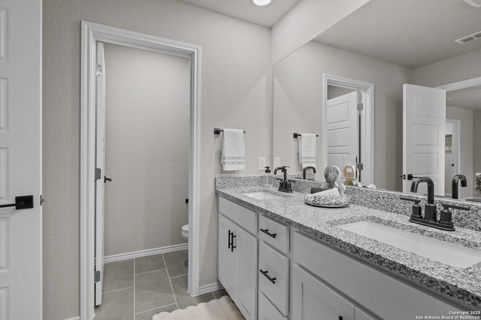 Modern master bathroom featuring double granite vanity, large mirrors, and neutral tile in Davidson Homes The Charlotte B, San Antonio