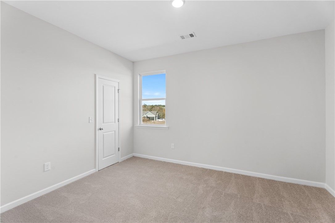 Bright secondary bedroom with gray walls, beige carpet, and window view in The Luna B by Davidson Homes, Opelika, Alabama