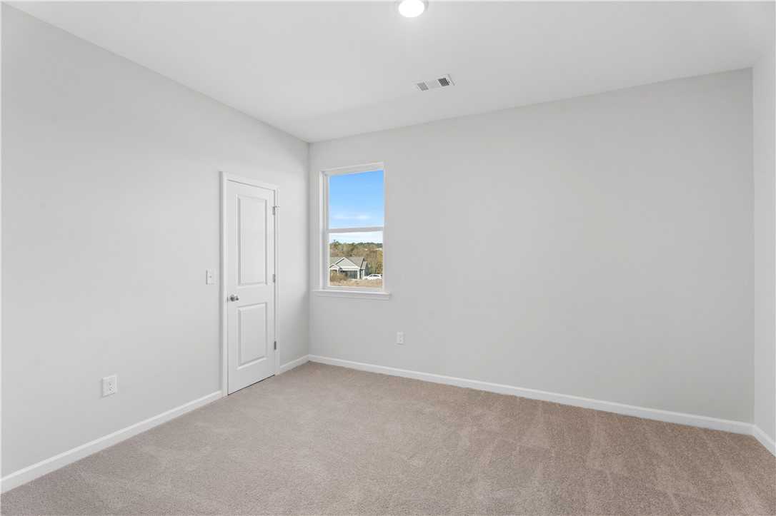 Bright secondary bedroom with gray walls, beige carpet, and window view in The Luna B by Davidson Homes, Opelika, Alabama