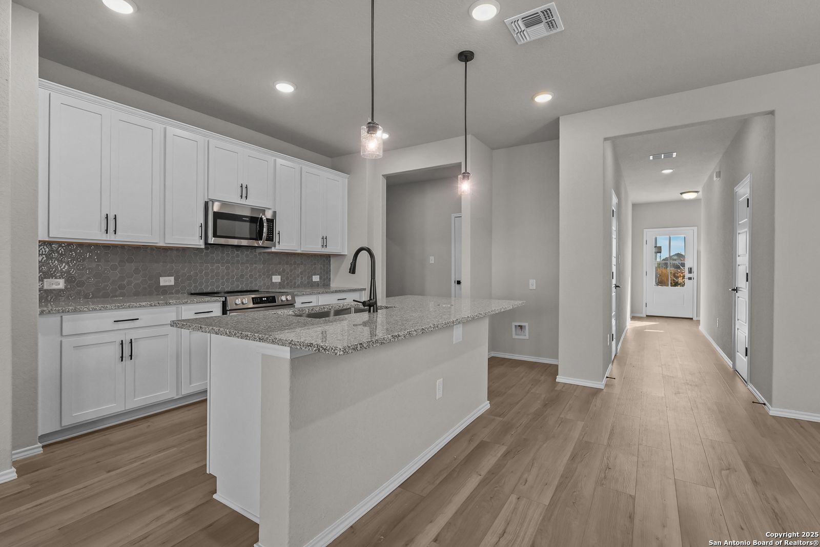 Open-concept kitchen with white cabinets, granite island, stainless appliances, and hardwood floors in Davidson Homes The Brazos C, San Antonio