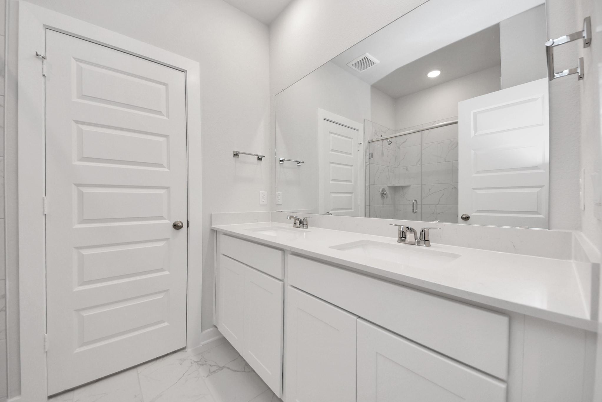 Modern primary bathroom with double vanity, white cabinetry, and glass-enclosed shower in The Sabine E, Windmill Estates.