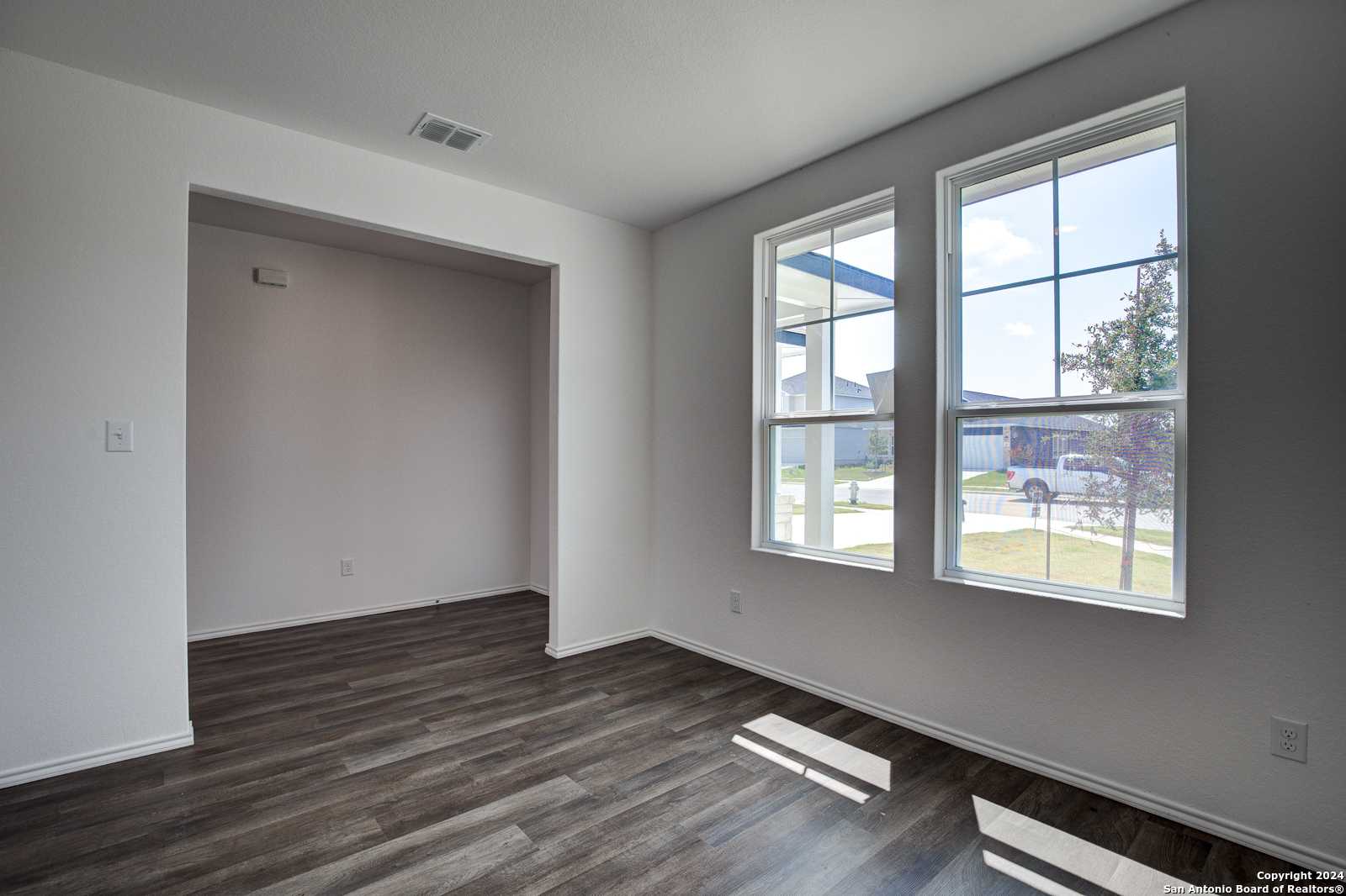 Bright living room with large sunny windows, hardwood floors, and open archway in Davidson Homes The Douglas D, Seguin, Texas