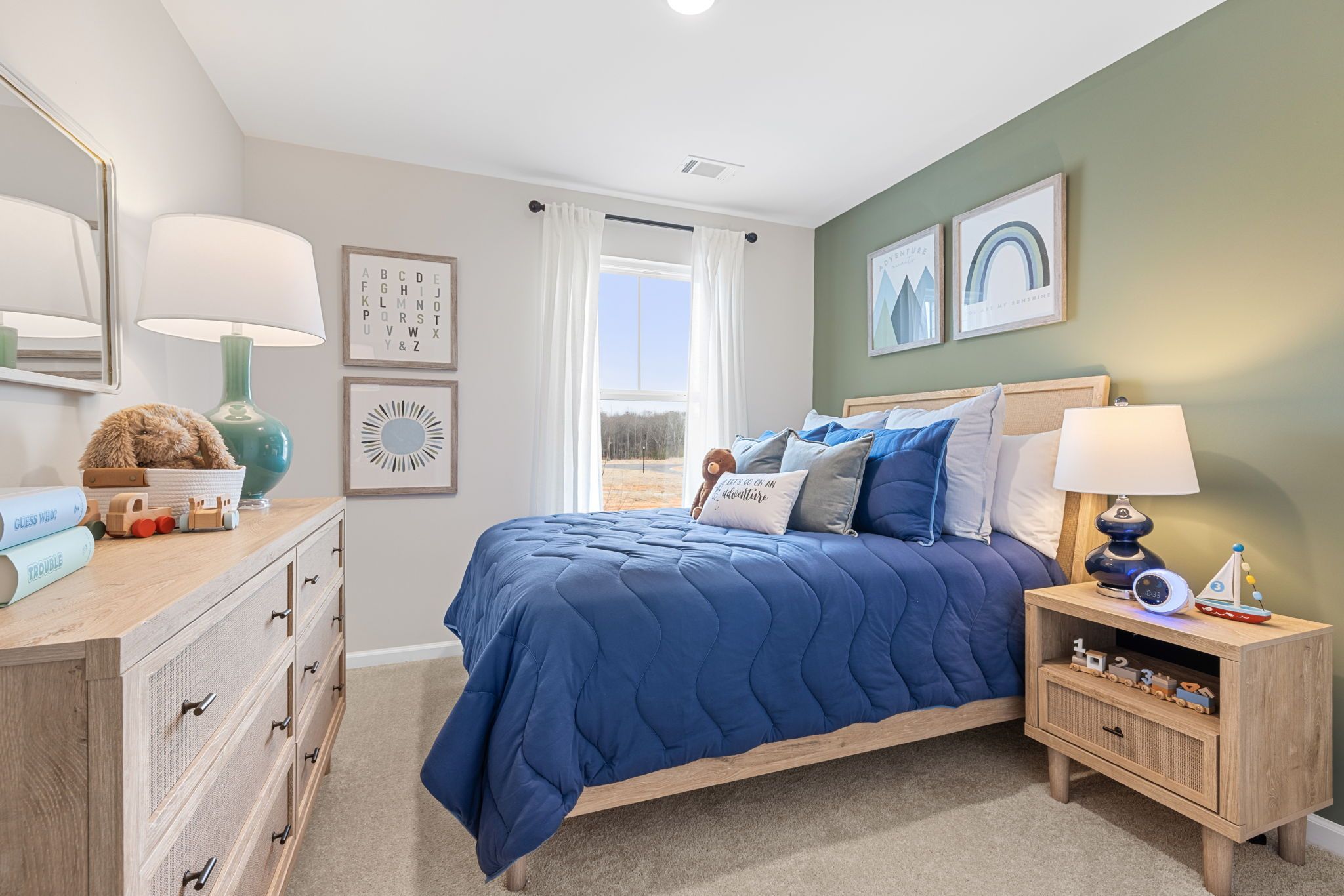 Boy's bedroom in Cedar Farms Winder Georgia with blue quilted bed, wooden dresser, toys, and green accent wall art