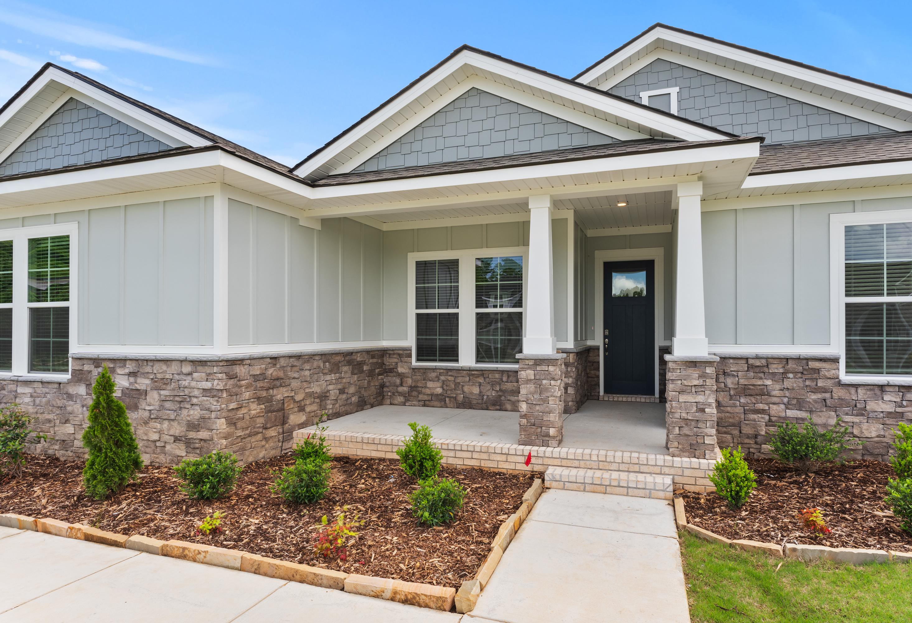 Front elevation of The Arcadia B single-story home with gray siding, stone base, gabled roof, and columned porch
