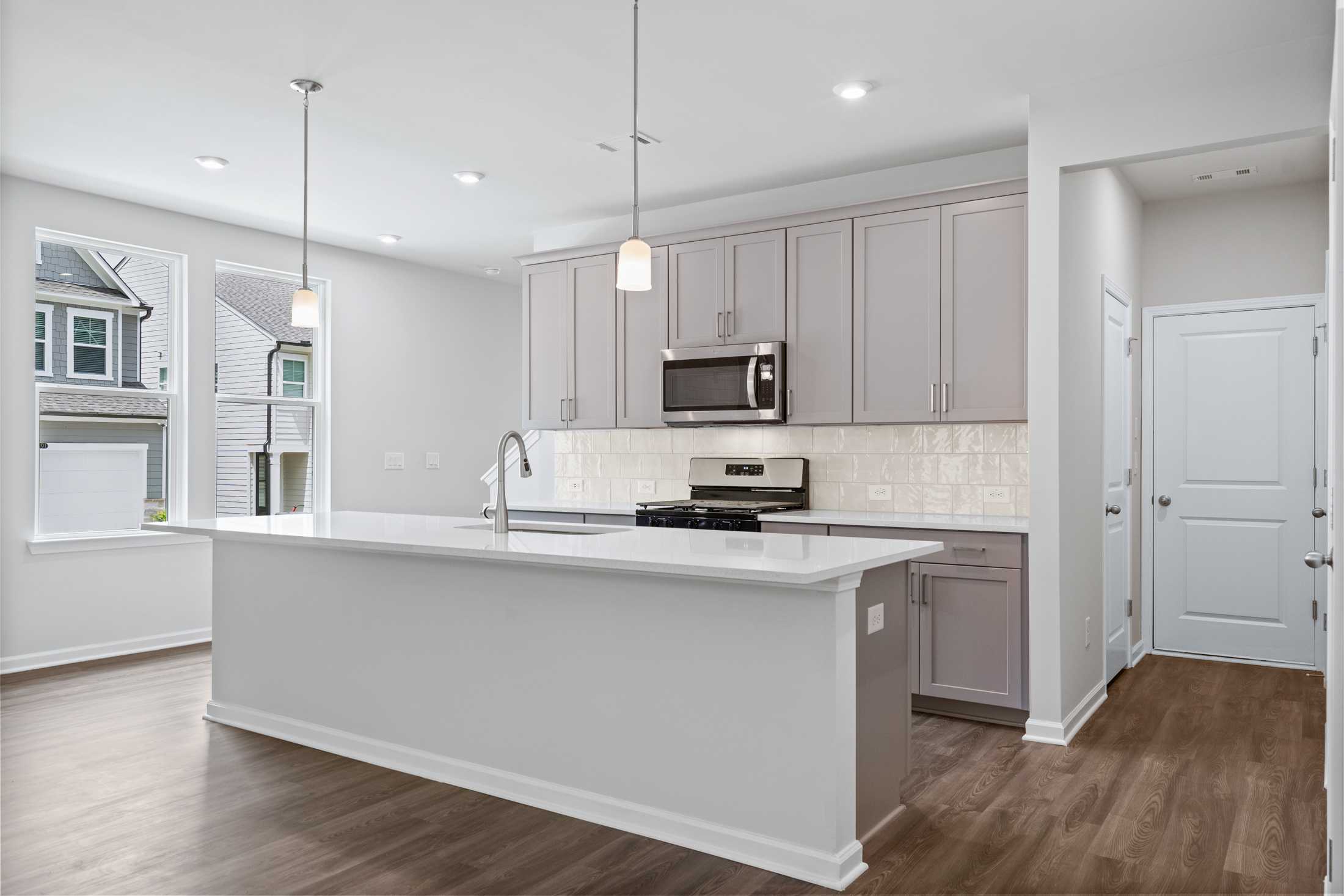 Bright kitchen in The Cary A with large white island, light gray cabinets, stainless steel appliances, subway tile backsplash, and hardwood floors