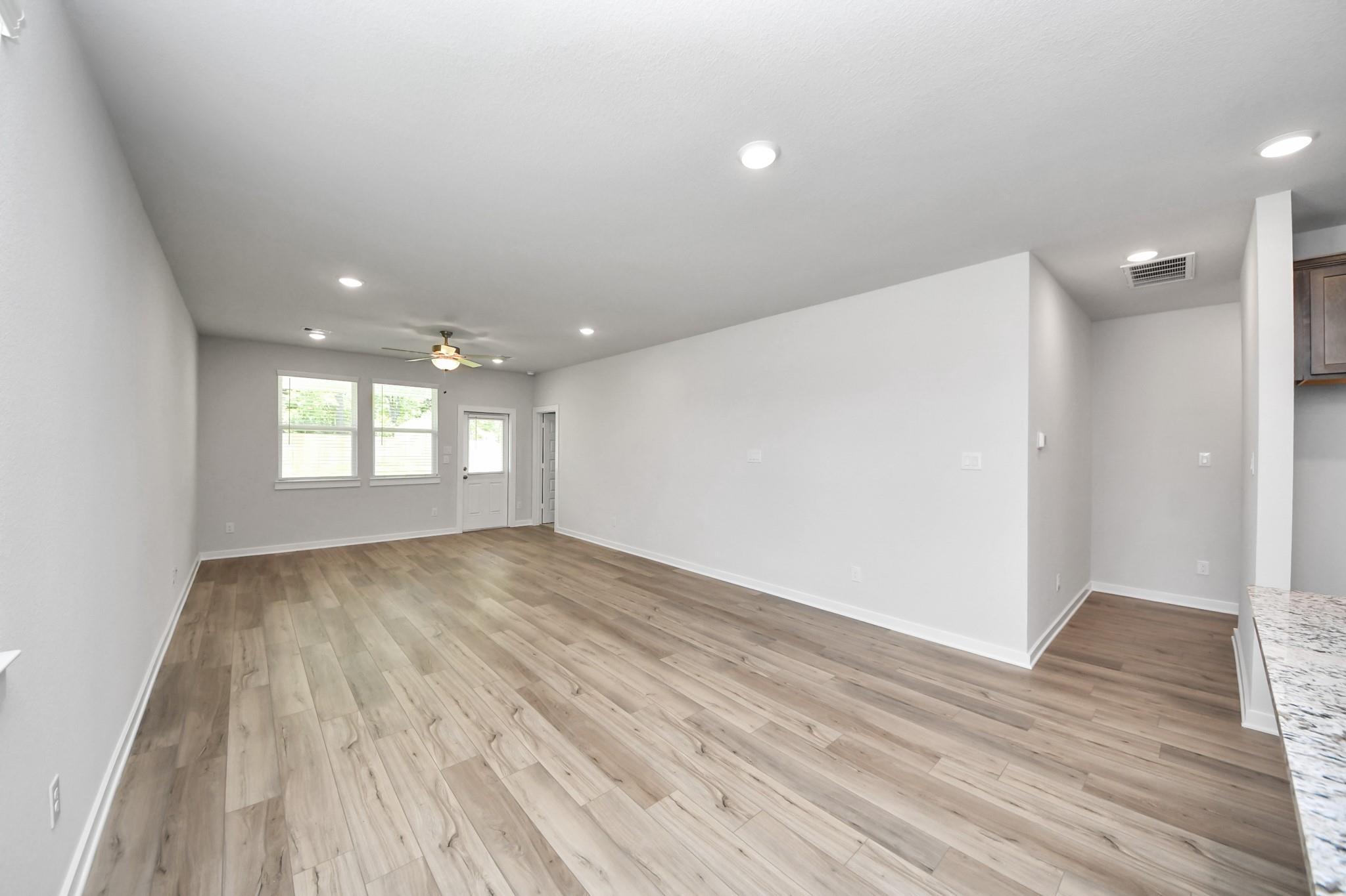 Spacious open-concept living room with wood-look flooring in The Sabine E floor plan at Liberty Estates, Cleveland, Texas.