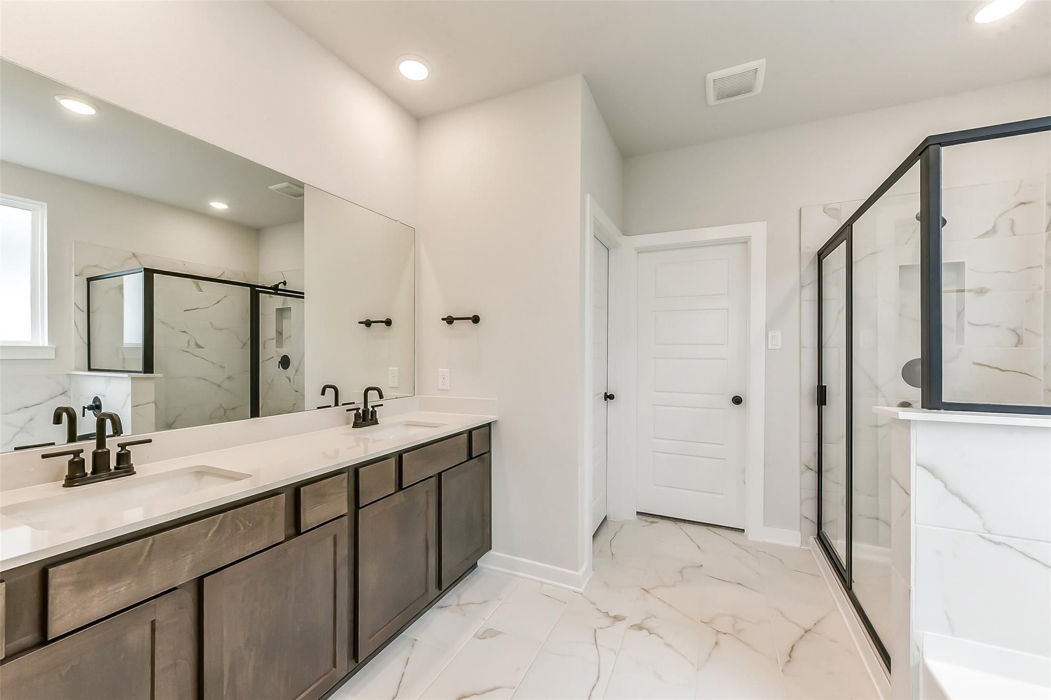 Elegant master bathroom featuring double vanity with quartz counters, marble tile shower, and bronze fixtures in Davidson Homes Sequoia C, Crosby TX