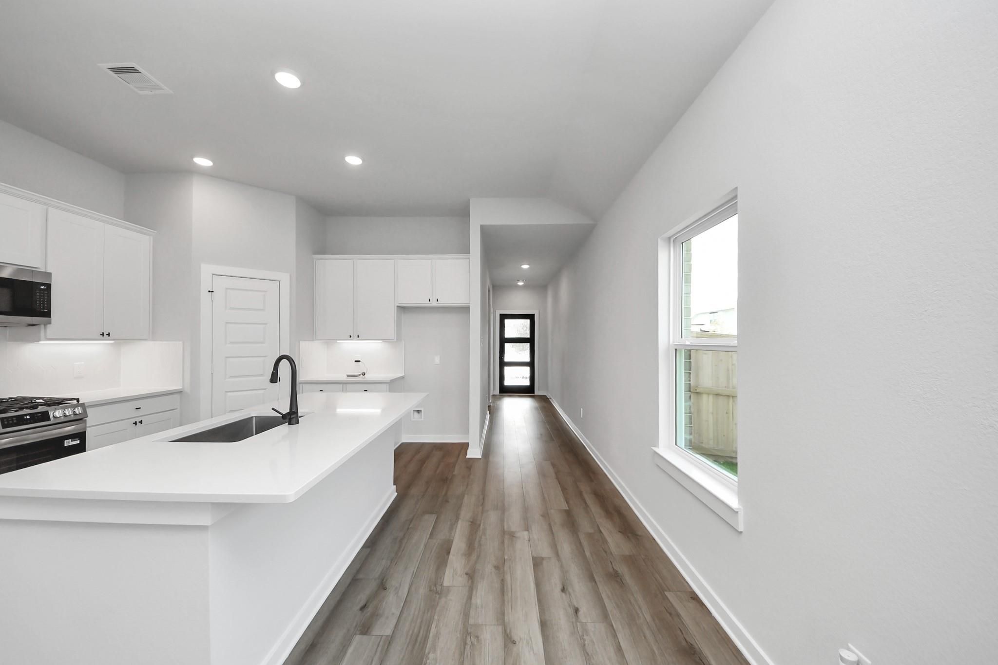 Modern kitchen with white cabinets, island, and wood-look flooring in The Riviera C floor plan, River Ranch Meadows, Dayton.