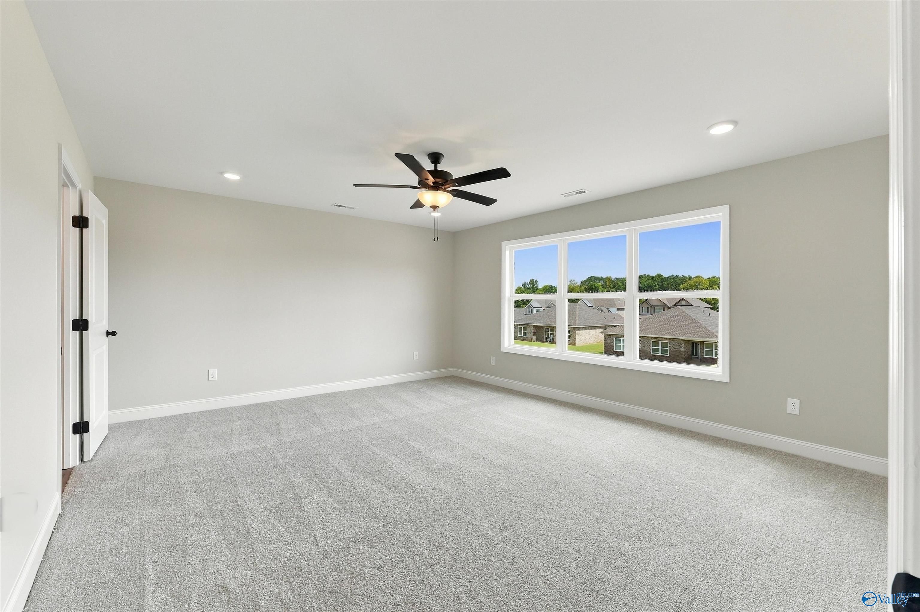 Spacious primary bedroom with gray carpet, ceiling fan, and large window views in Davidson Homes The Shelby A, Athens, Alabama