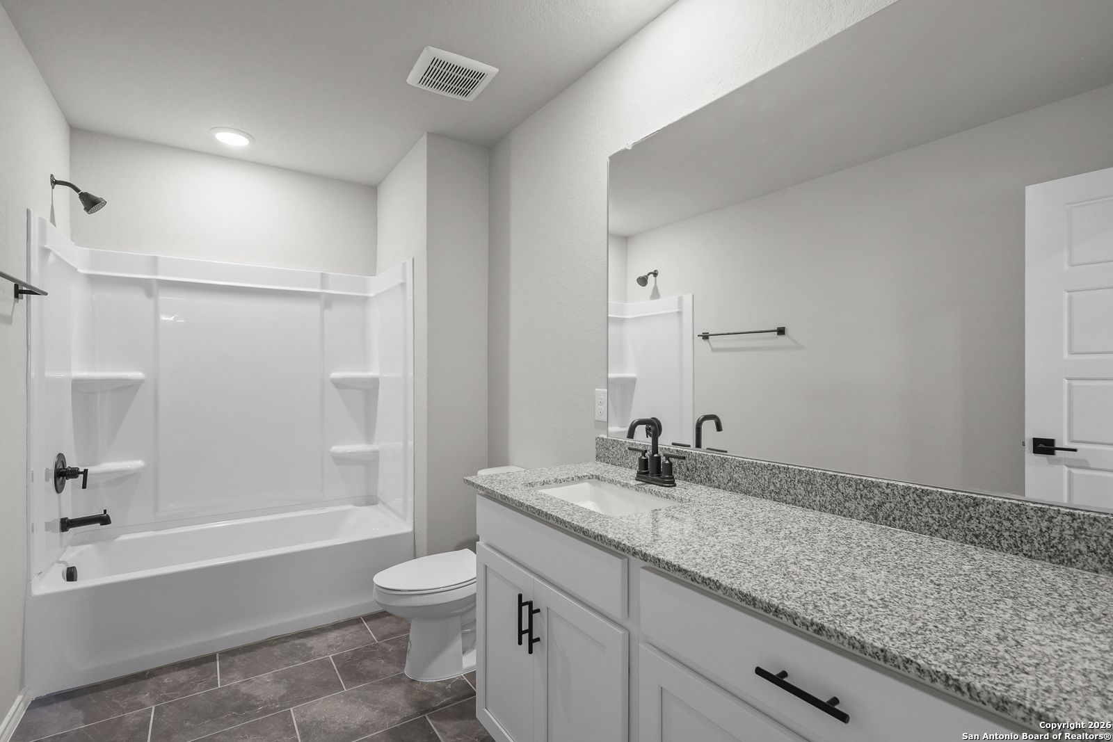 Bright bathroom with white tub-shower, granite vanity, mirror, and tile floor in Davidson Homes The Murray K, San Antonio