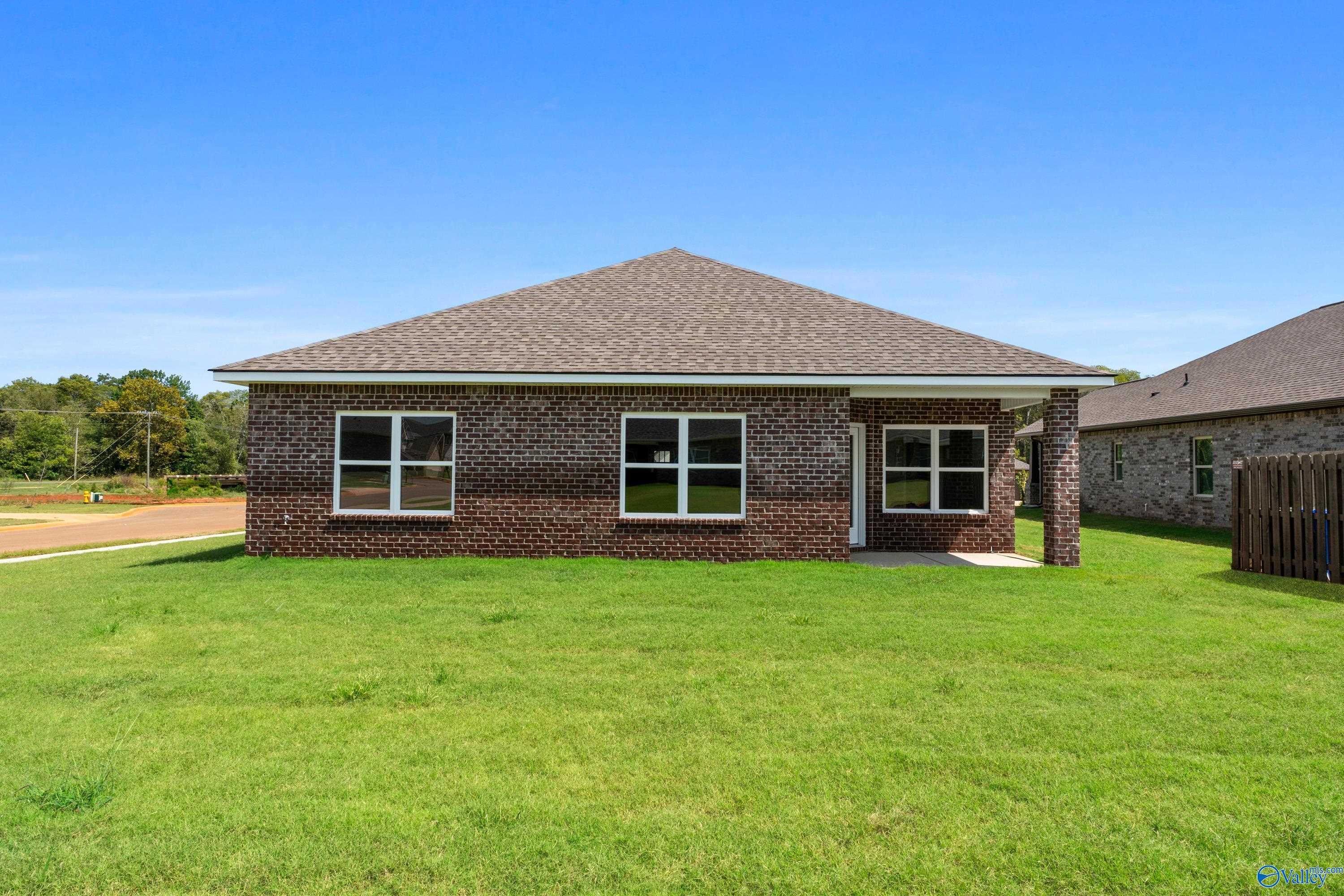 Brick 1-story 4-bedroom home with attached garage, lush green lawn, and blue sky in The Meadows, Athens, Alabama