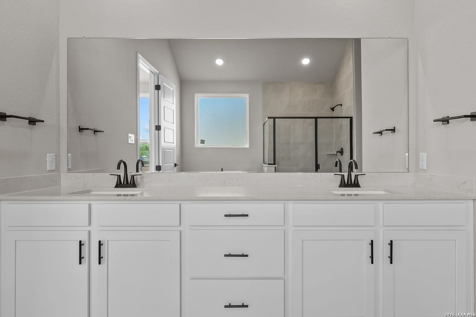 Dual vanity bathroom with white shaker cabinets, quartz countertops, matte black faucets, and large mirror in Davidson Homes Foster E plan